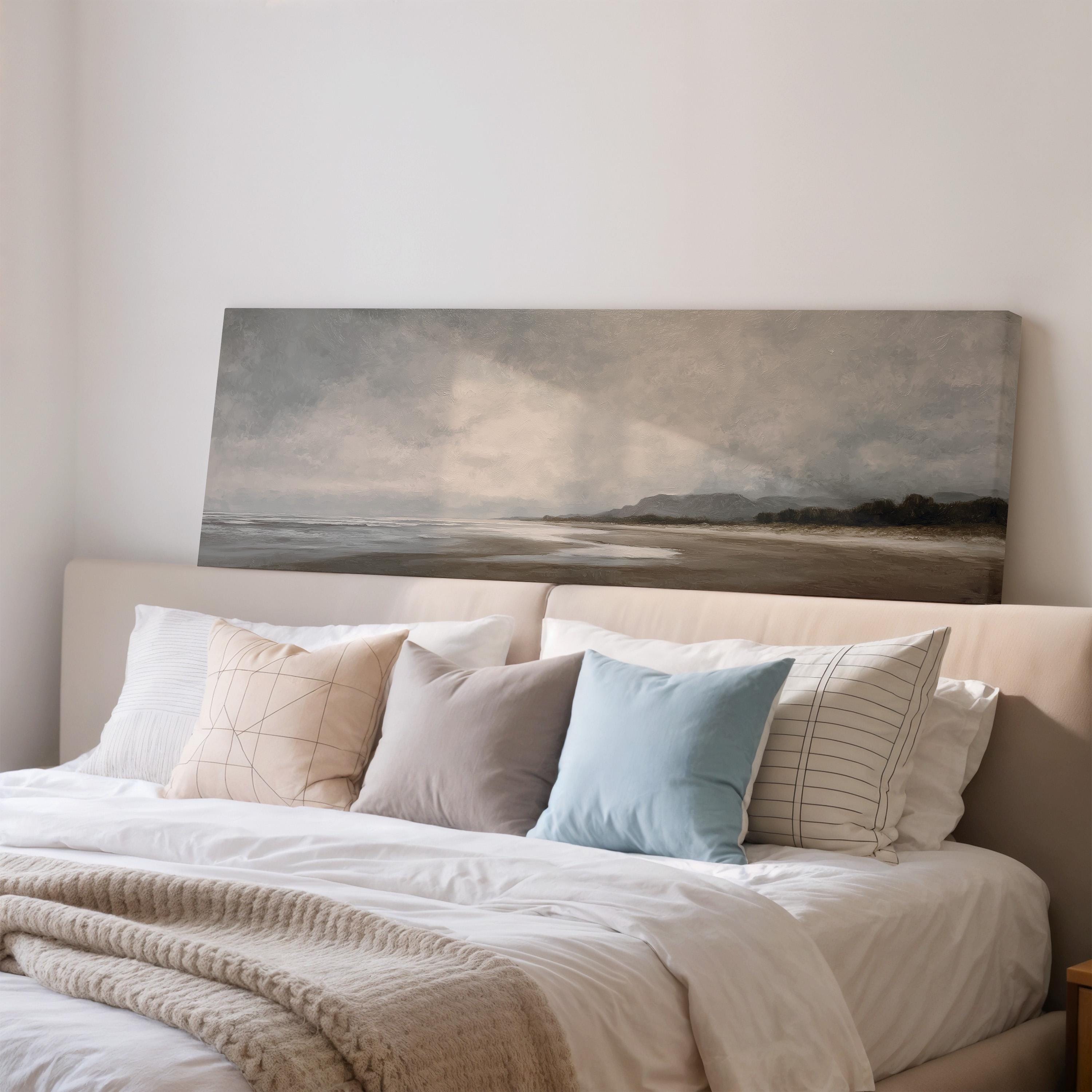 a bedroom with a large bed adorned with white linens and a blue pillow. Above the bed, there is a painting of a beach scene with mountains in the background.
