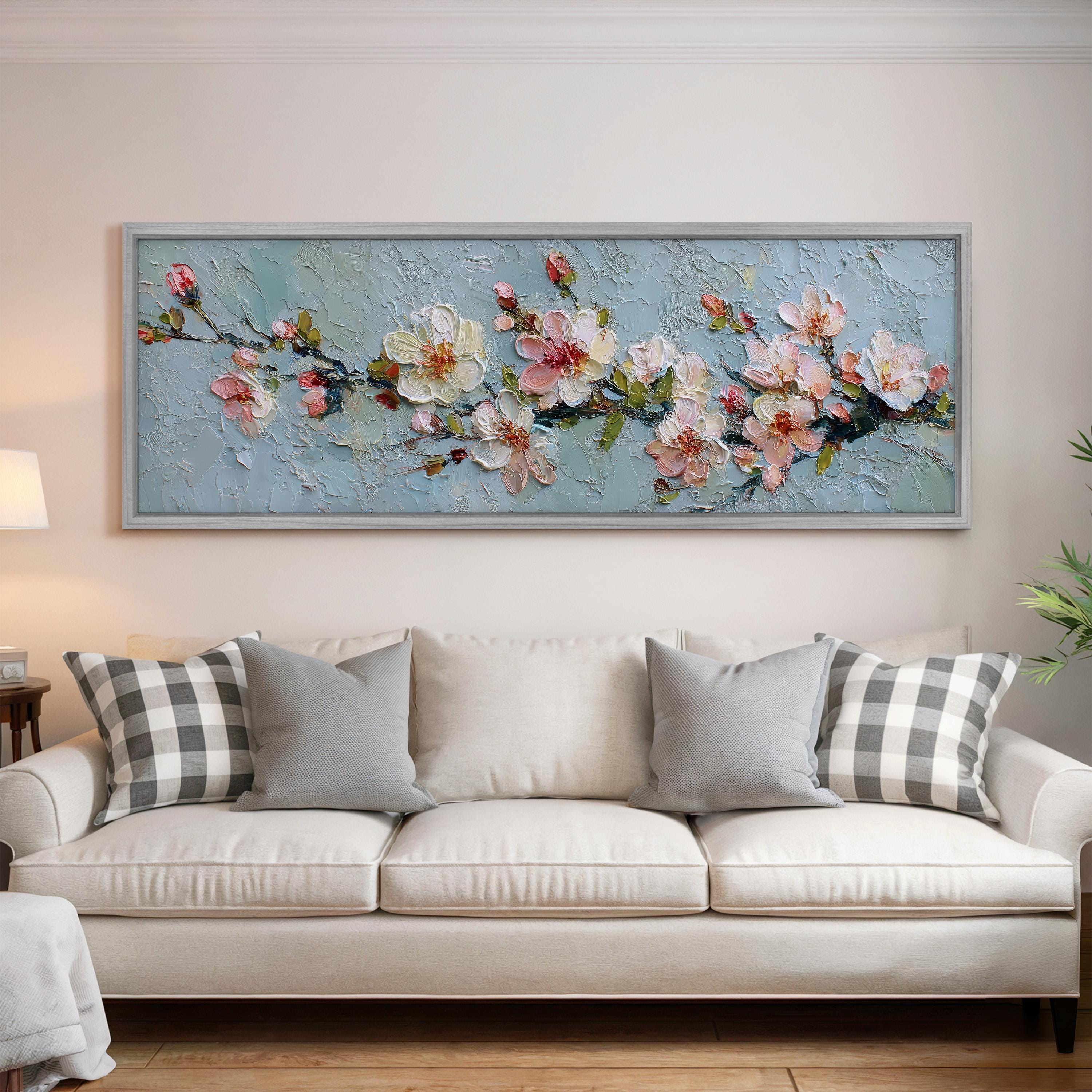 a large painting of flowers hanging on a wall above a white couch with gray and white plaid throw pillows.