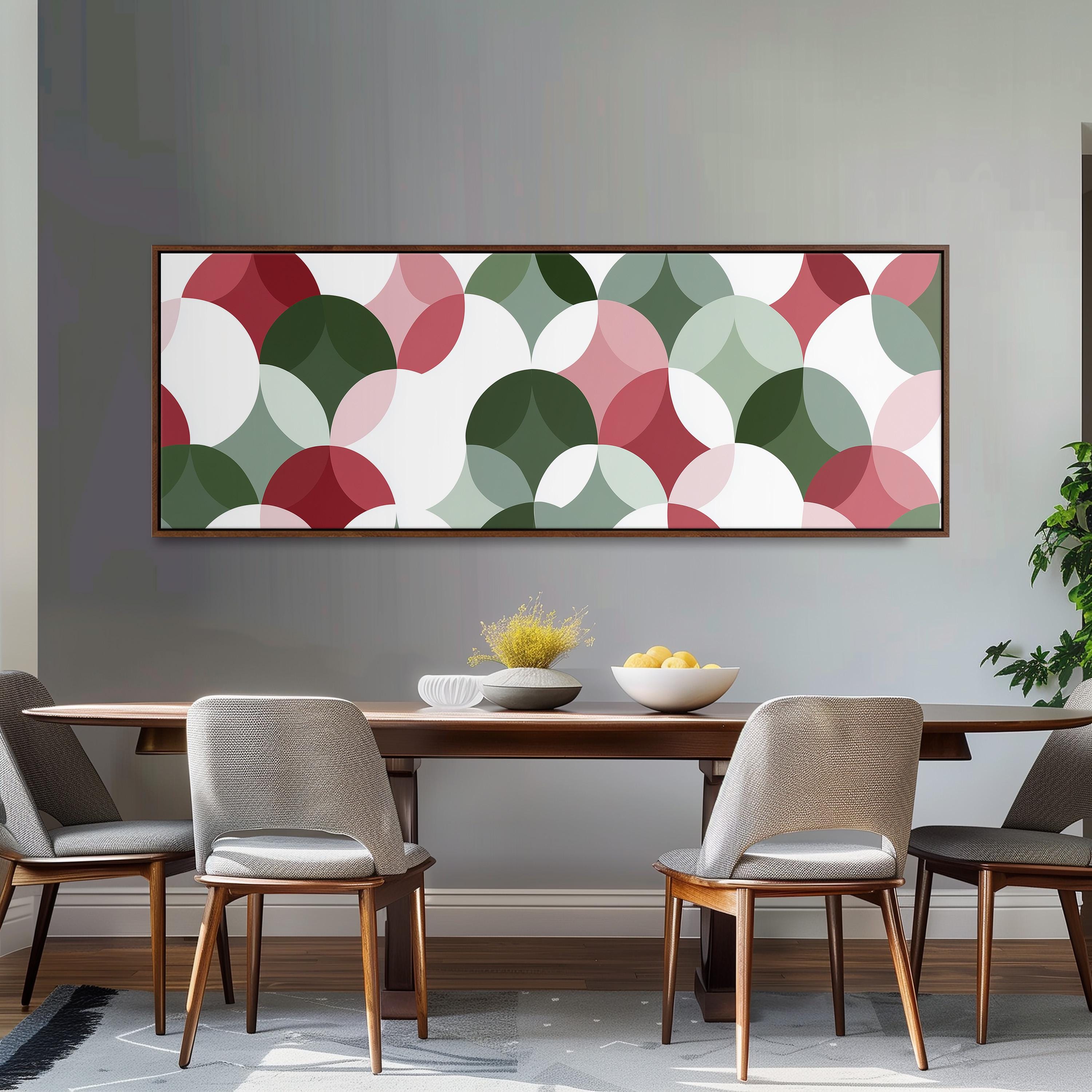 a modern dining room with a wooden table and four chairs. Above the table, there is a large abstract painting with a colorful design of overlapping circles in various shades of green, pink, and white. The painting is framed and hangs on the wall above the dining area.