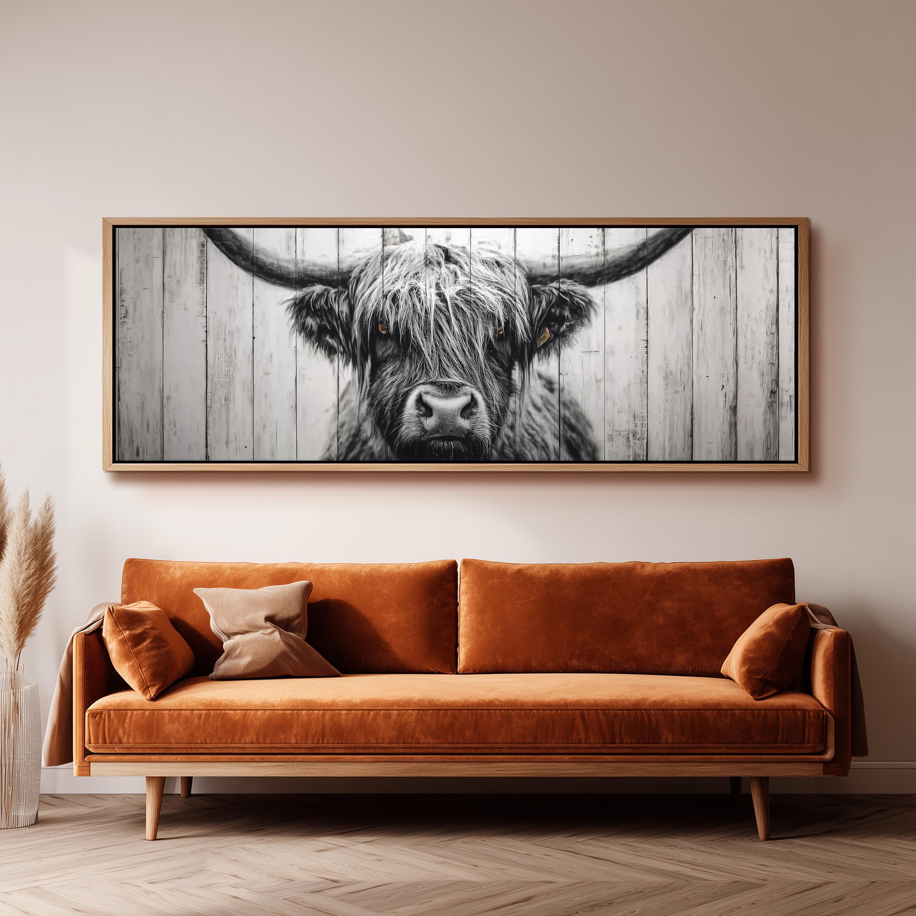 a large black and white photograph of a cow's head with long horns, hanging on a wall above a brown sofa.