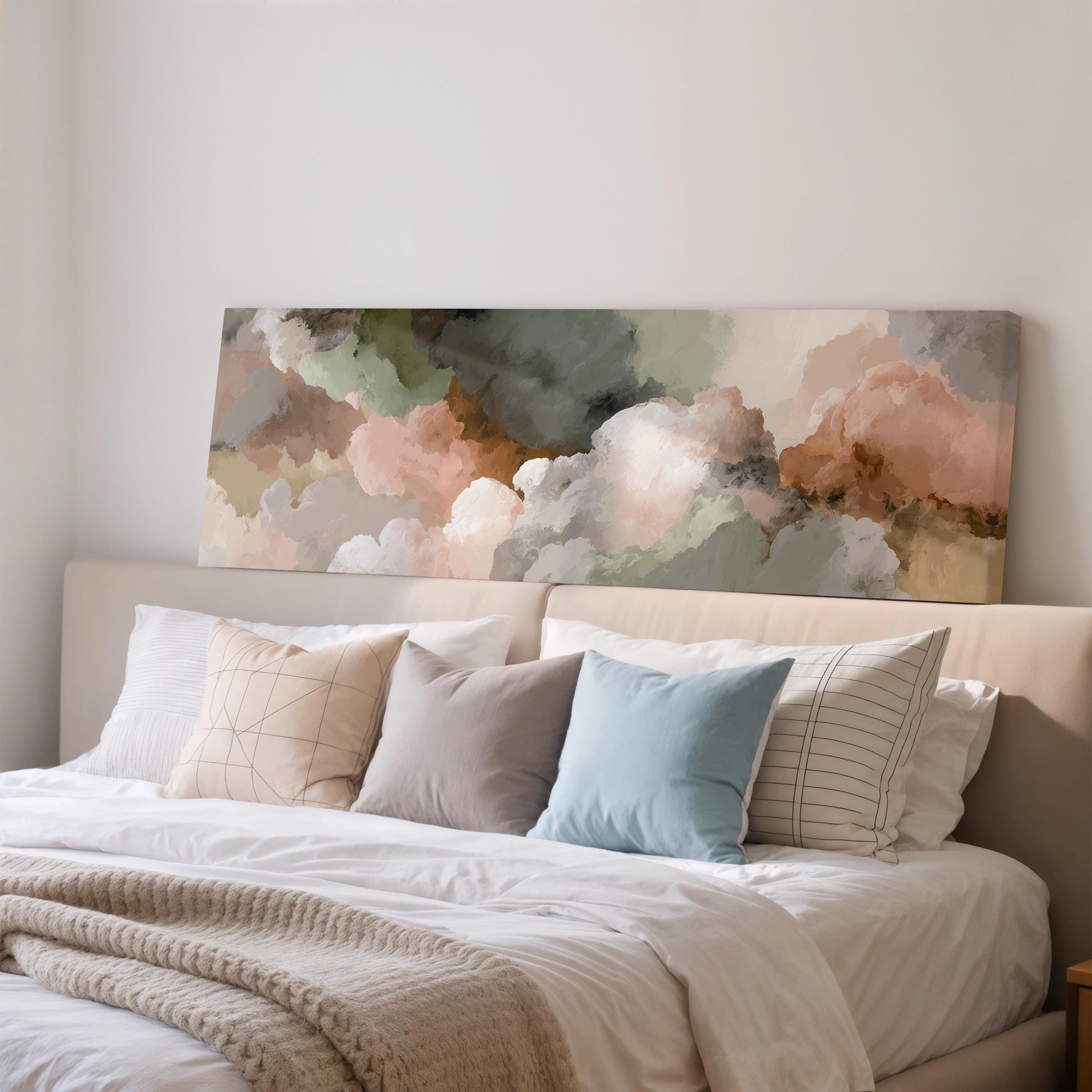 a large bed with a white comforter and a variety of colorful pillows. Above the bed, there is a large canvas print depicting a cloudy sky with a mix of green, pink, and gray colors.