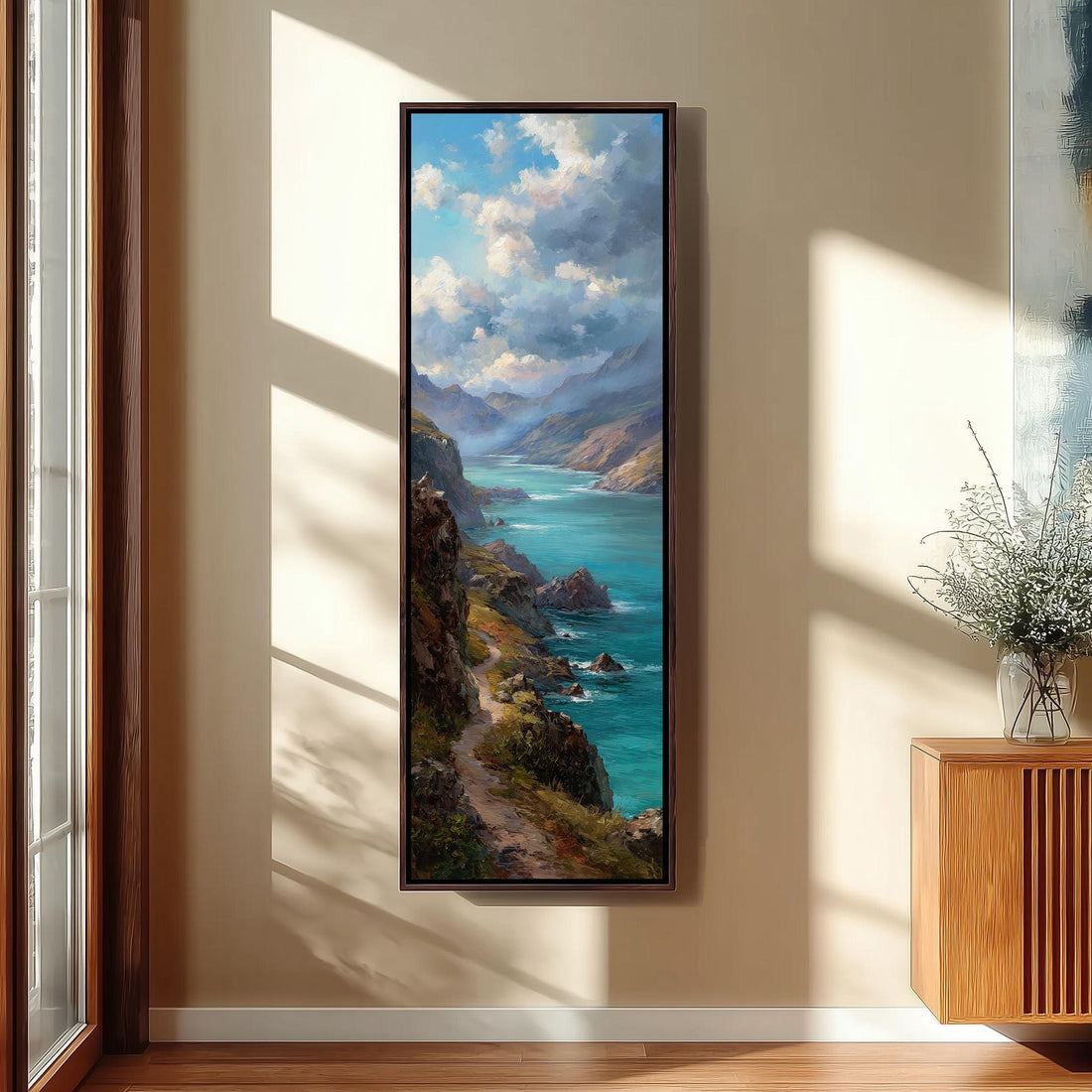 a large framed painting of a scenic coastal landscape, with a winding path leading to a turquoise sea and mountains in the background.