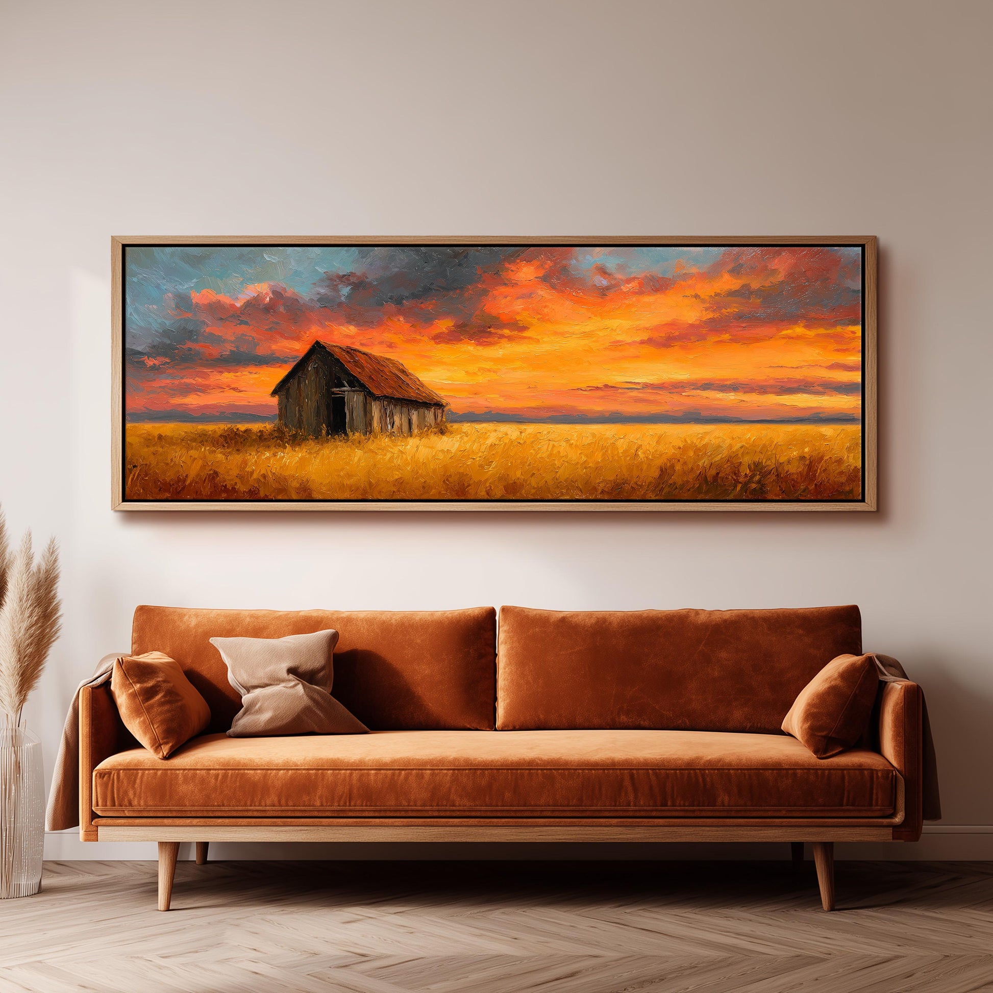 a large painting of a barn and a field with a colorful sunset sky above it, hanging on a wall above a brown sofa.