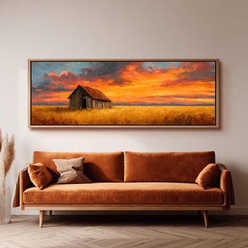 a large painting of a barn and a field with a colorful sunset sky above it, hanging on a wall above a brown sofa.