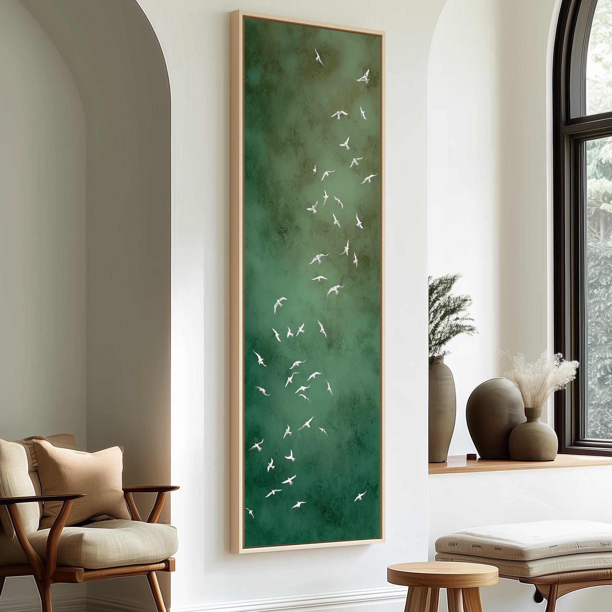 a large green painting hanging on a white wall, depicting a flock of white birds in flight. The painting is framed and placed above a seating area with a wooden chair and a small table.