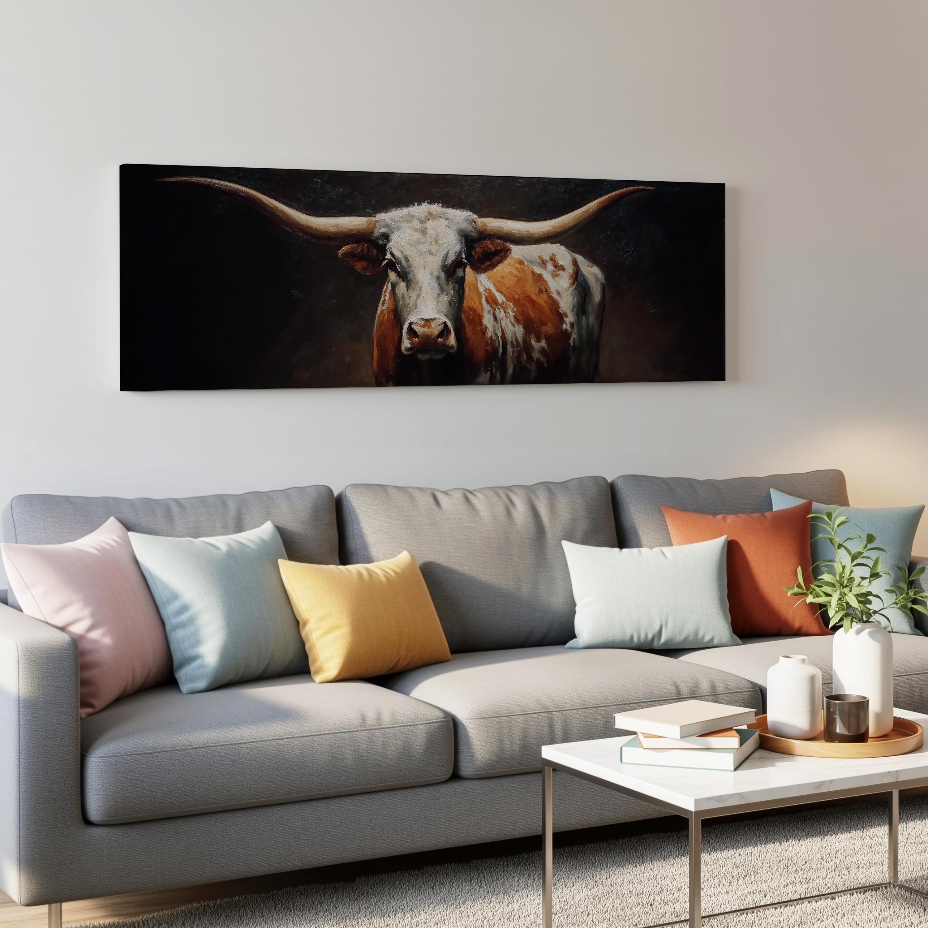 a large painting of a bull with long horns hanging on a wall above a gray couch with colorful throw pillows.