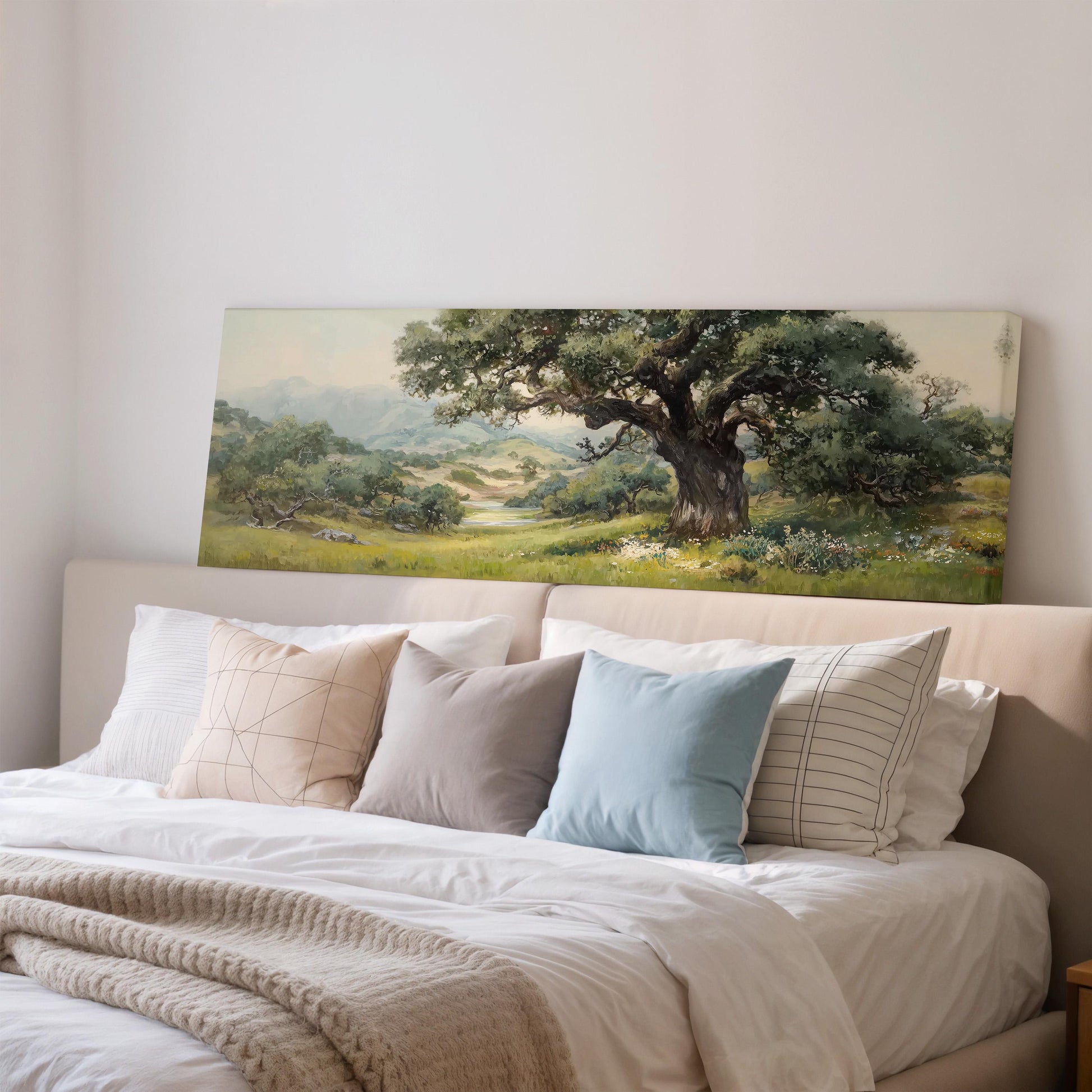 a large painting of a lush green landscape hanging on a wall above a bed with white bedding and pillows.