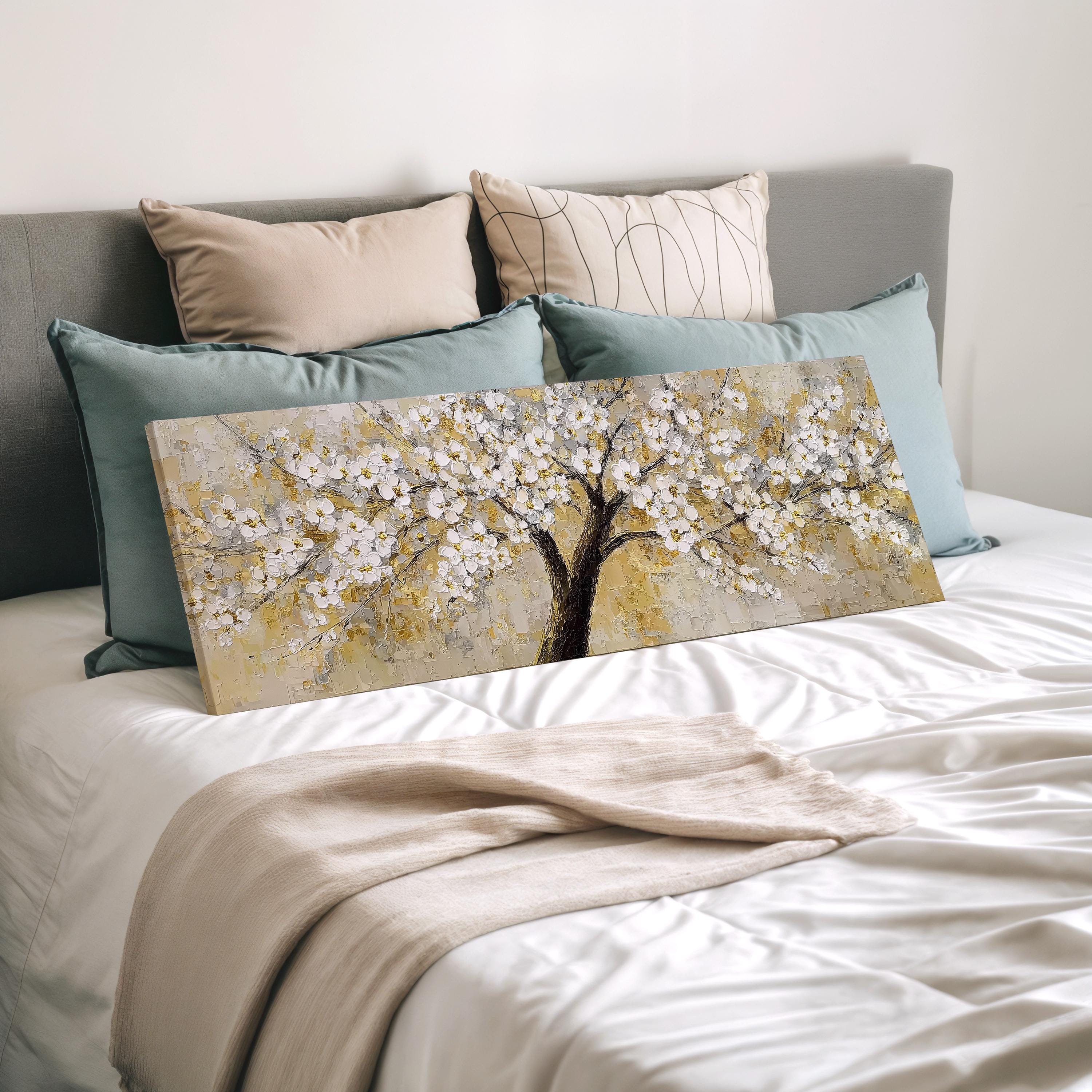 a large painting of a tree with white flowers on a bed, surrounded by various pillows and blankets.