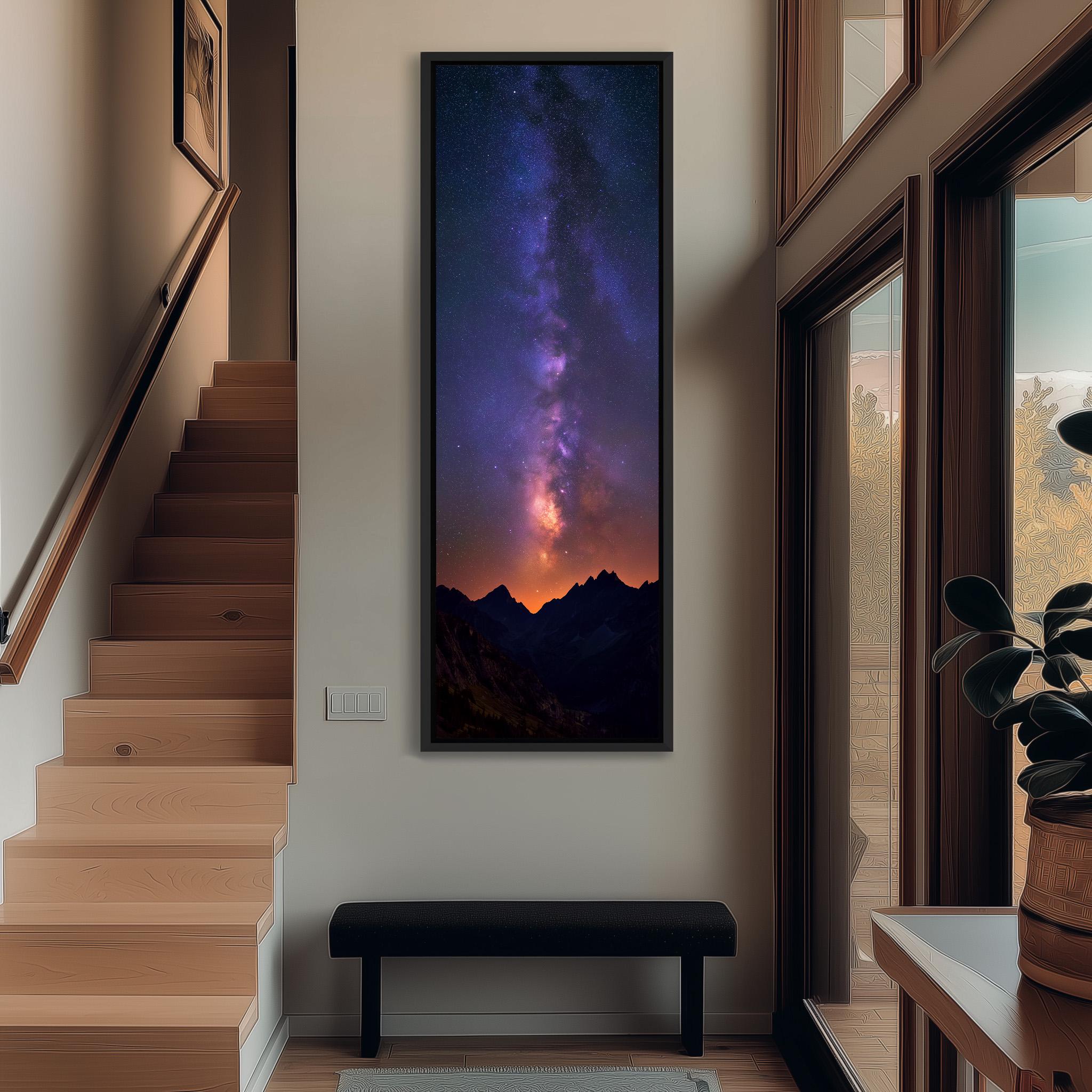 a large, framed picture of a night sky with a galaxy, hanging on a wall in a hallway. The hallway has a wooden staircase and a bench, and there is a plant on the right side of the image.