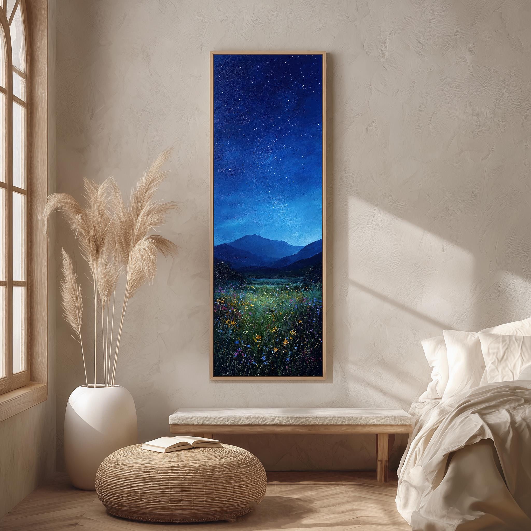 a serene bedroom scene with a large painting of a night sky with stars hanging on the wall, a white bed with a white pillow, a white vase with tall potted plants, and a woven ottoman in front of the bed.