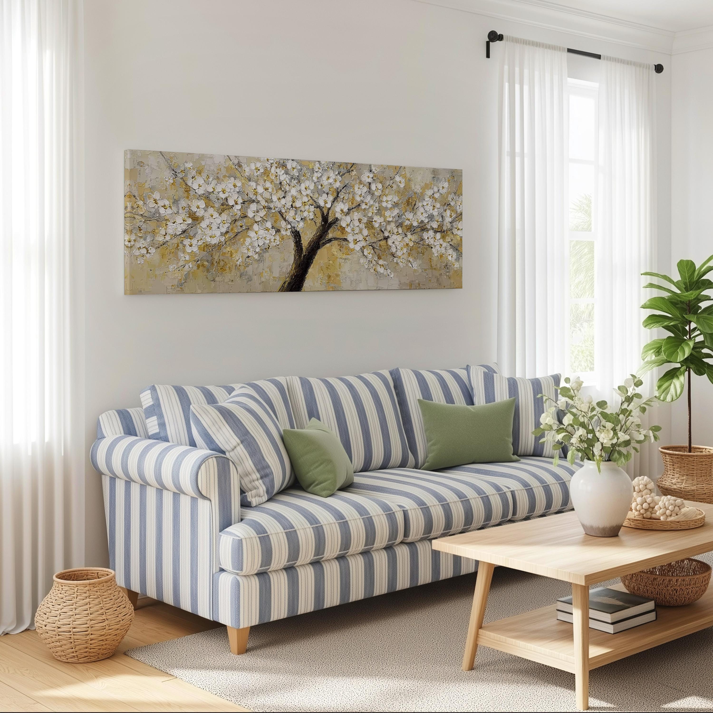 a cozy living room with a striped blue and white sofa, a wooden coffee table, and a large painting of a tree with white flowers hanging on the wall above the sofa.