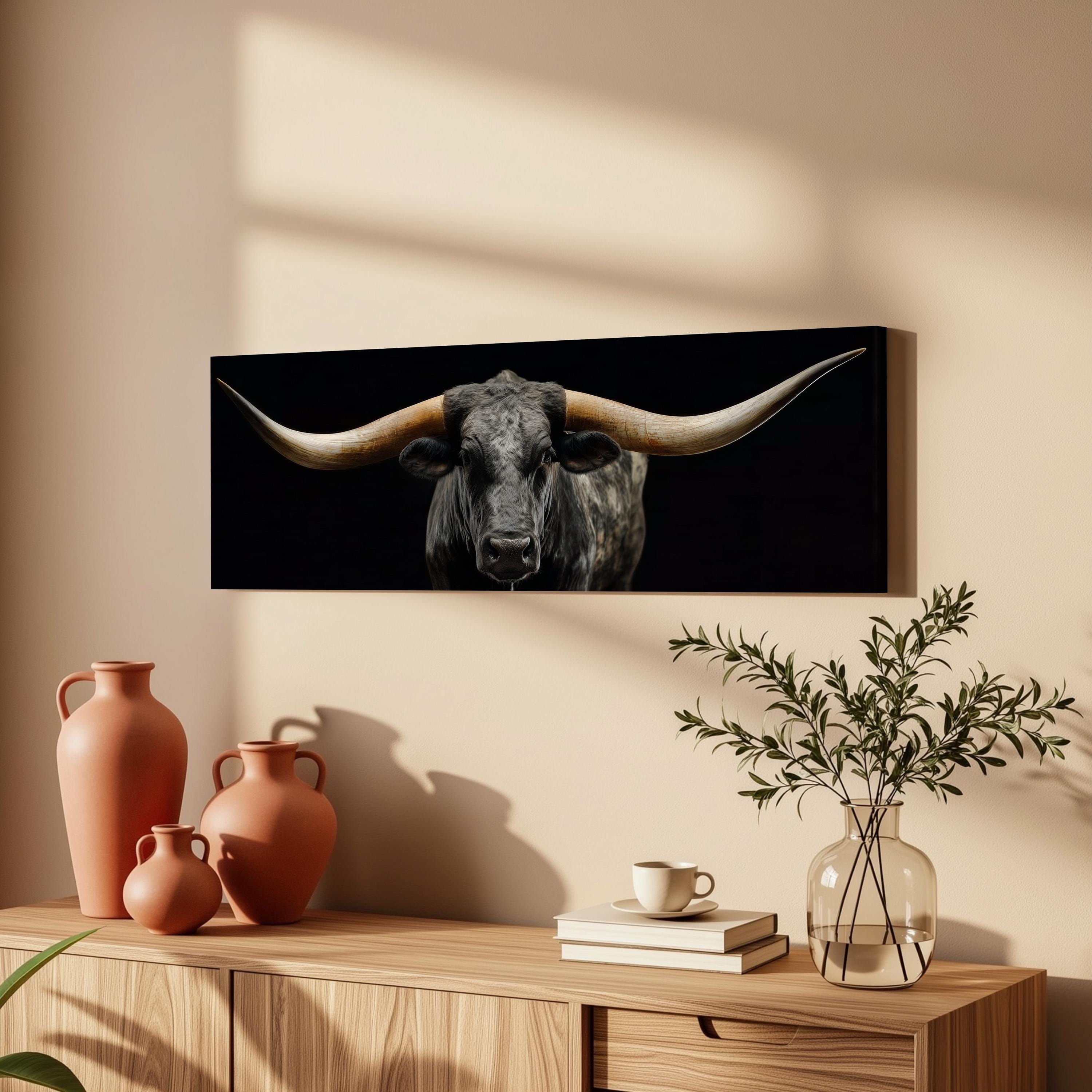 a large black bull with long horns, displayed on a wall above a wooden cabinet. The bull is the central focus of the image, with a vase and a plant placed on the cabinet below it.