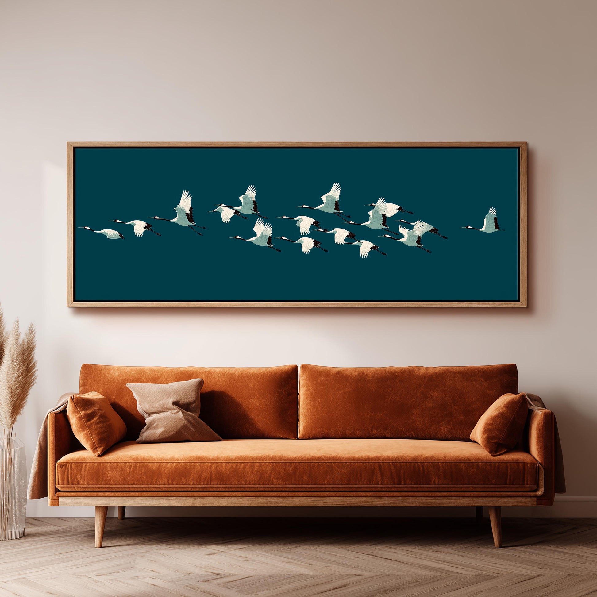 a large framed artwork of a flock of white birds flying over a dark blue background, hanging on a wall above a brown sofa.