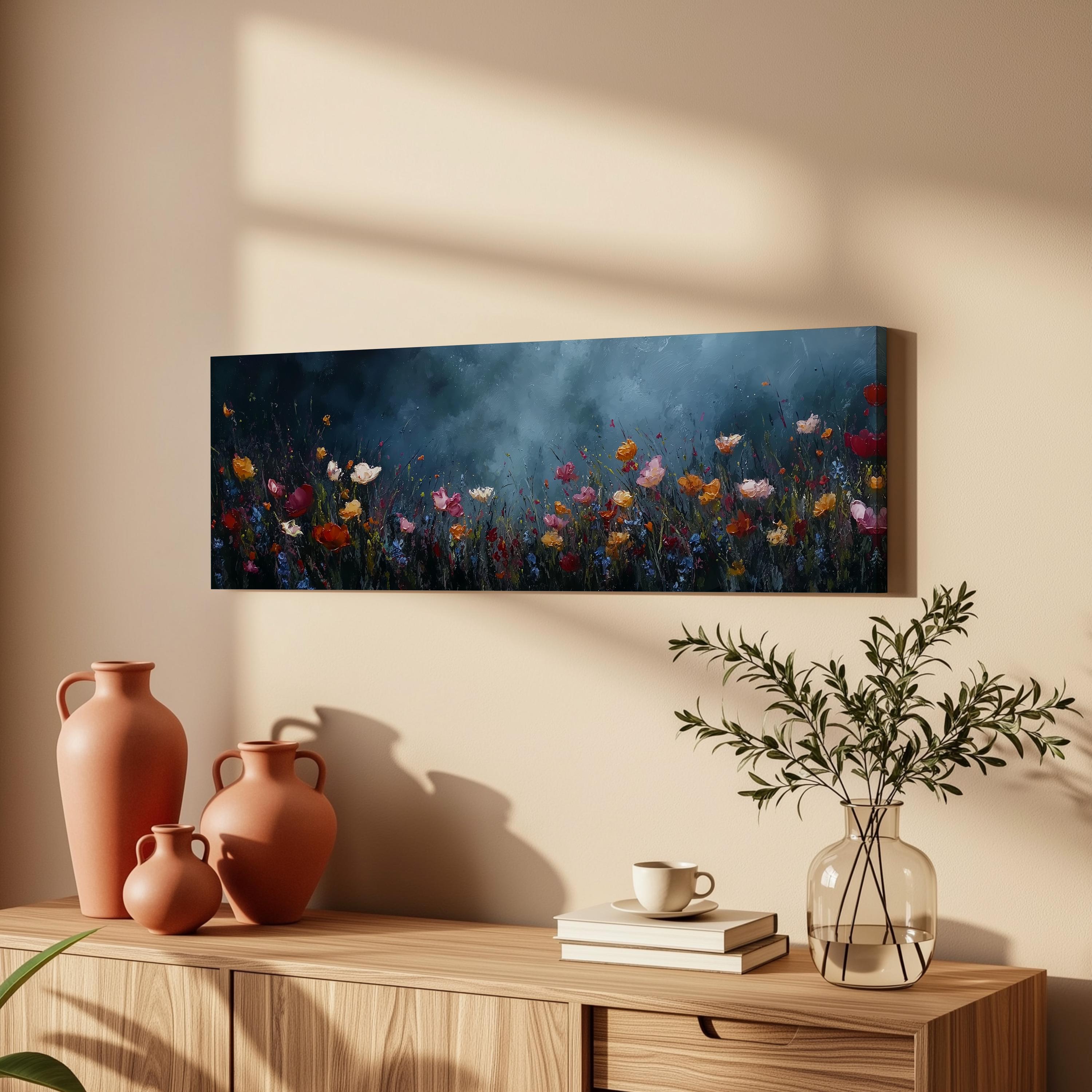 a wooden cabinet with a vase of greenery, a coffee cup, and a stack of books on top. Above the cabinet, there is a painting of a field of flowers.