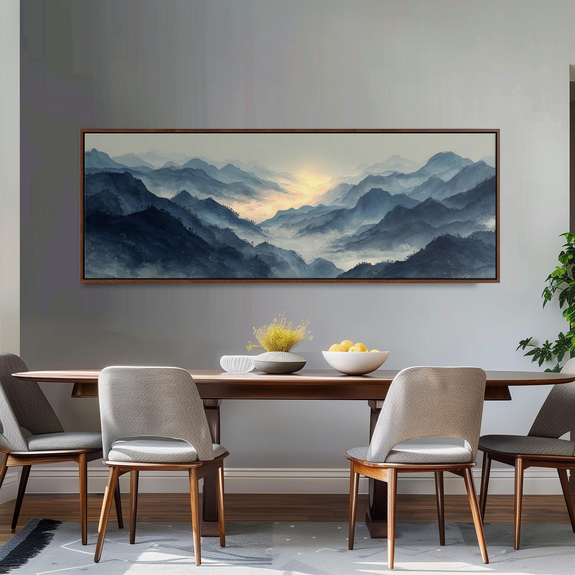 a dining room with a large painting of a mountain landscape hanging on the wall above a wooden dining table with four chairs. The painting depicts a serene mountain scene with a warm, golden glow at the horizon.