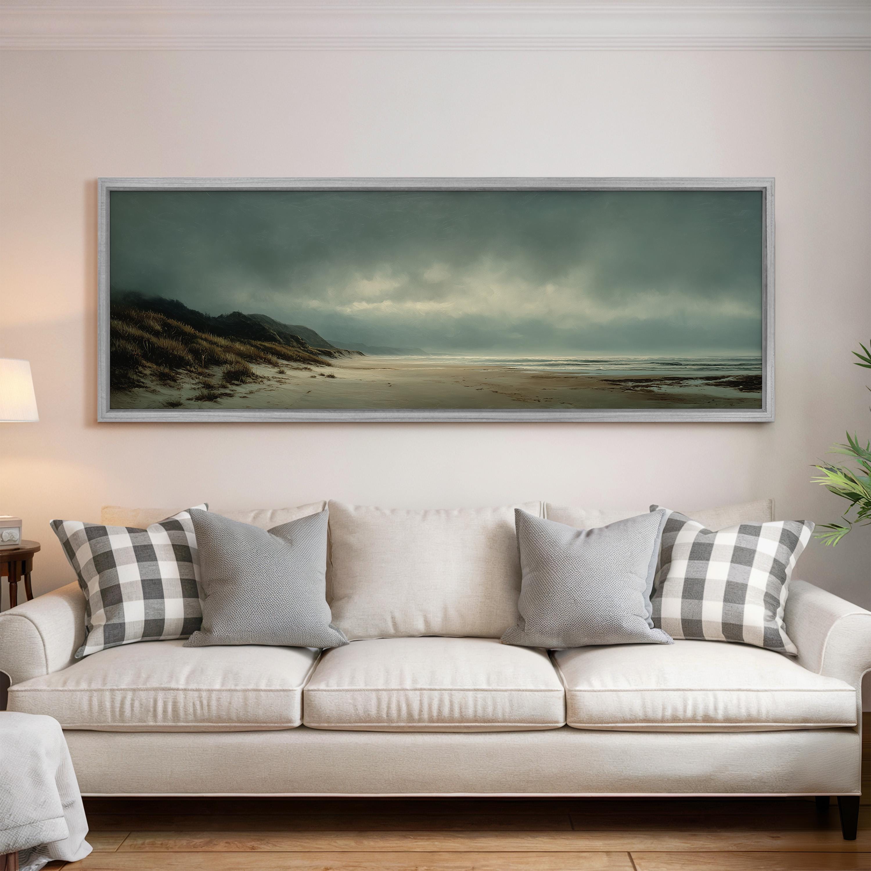 a large, framed painting of a beach scene hanging on a wall above a white sofa with gray and white patterned pillows.