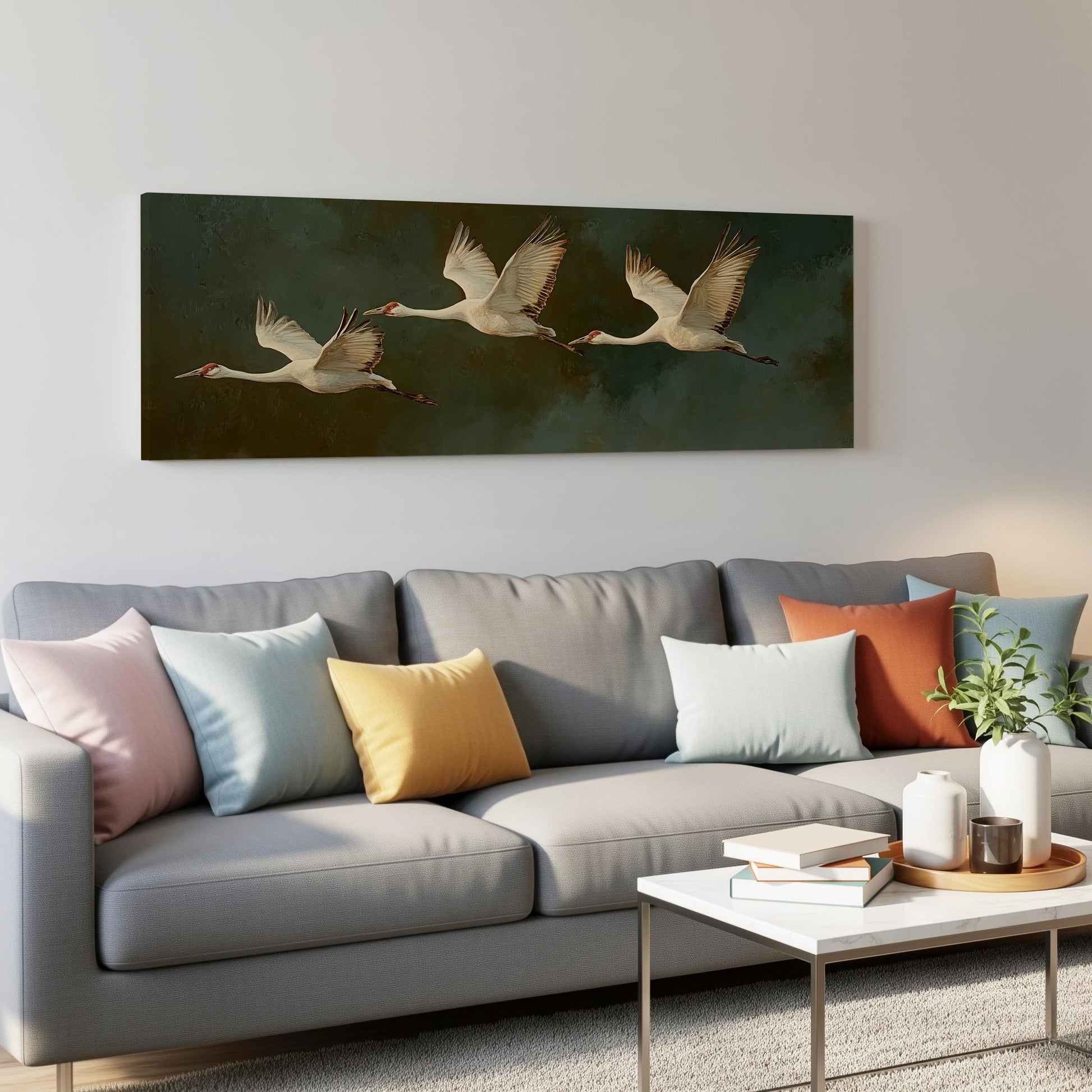 a gray couch with colorful throw pillows, a coffee table, and a painting of three white birds in flight on the wall above it.