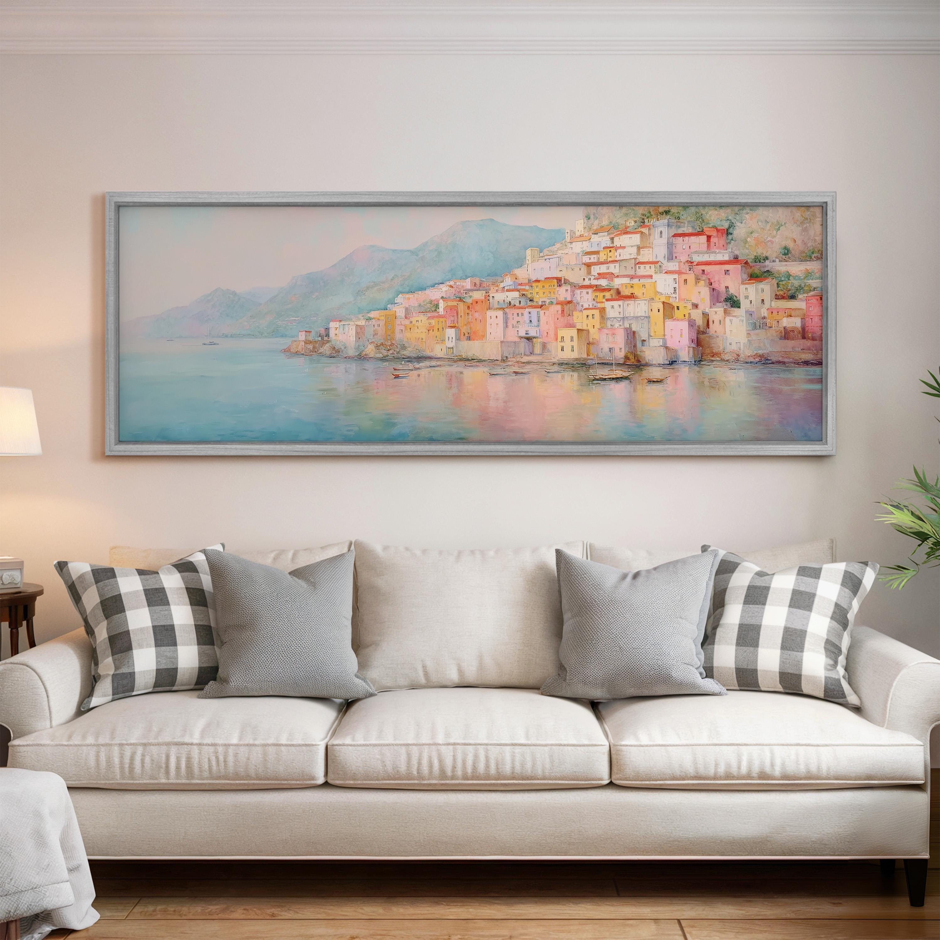 a large, colorful painting of a coastal town hanging on a wall above a white couch with gray and black checkered throw pillows.