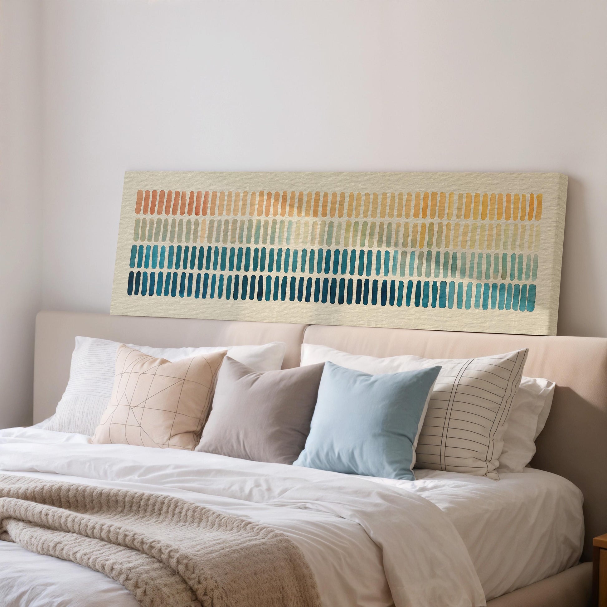 a well-made bed with a white comforter and various pillows in different colors and patterns. Above the bed, there is a large abstract painting or artwork featuring vertical lines in various colors.