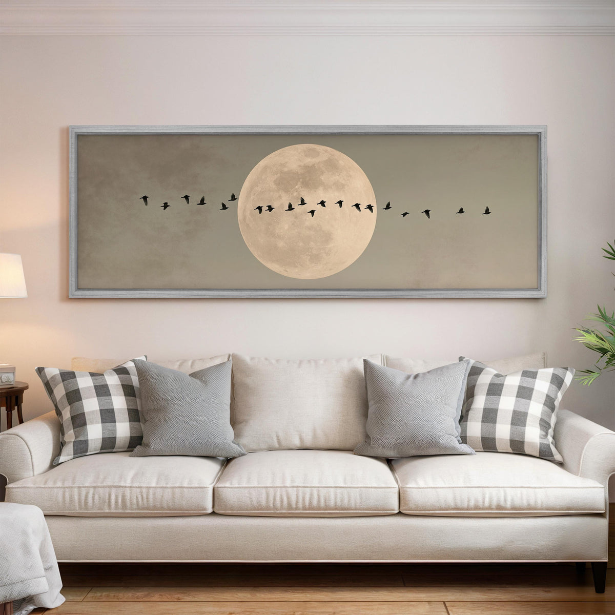 Geese crossing a full moon on grey panoramic canvas print above a white sofa in a bright living room