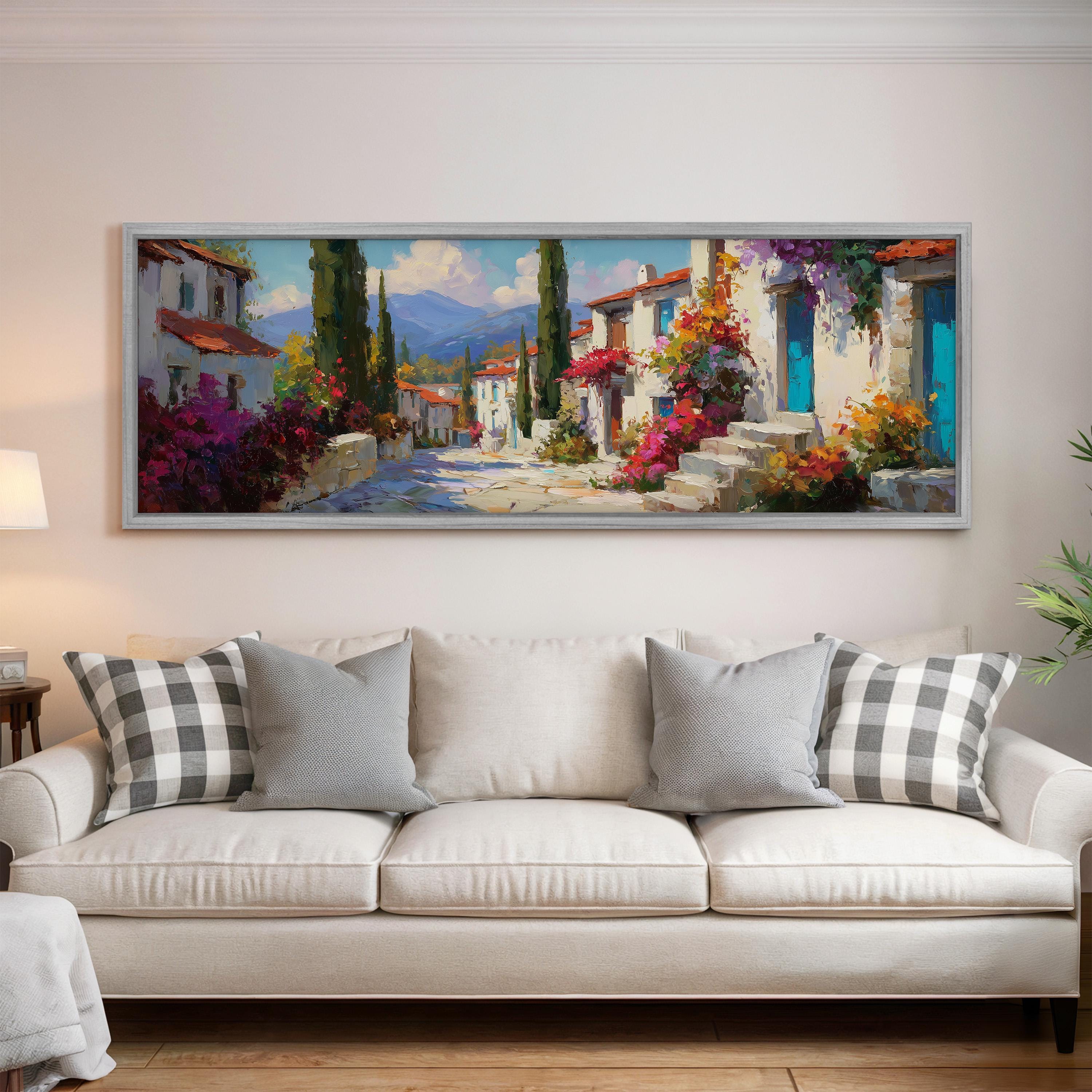 a large, colorful painting of a picturesque village scene hanging on a wall above a white sofa with gray and white patterned pillows.