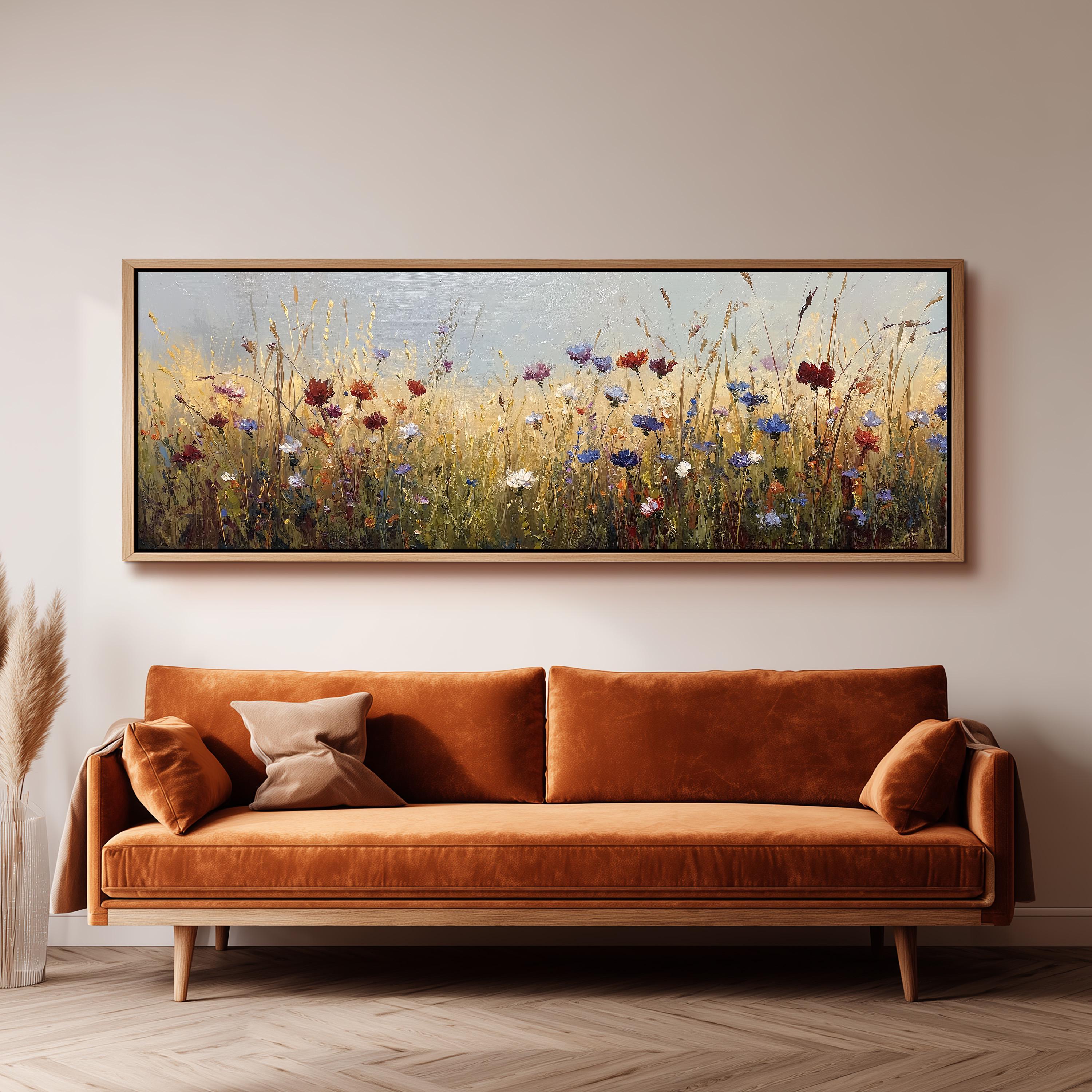 a large, framed painting of a field of flowers hanging on a wall above a brown sofa with orange cushions.