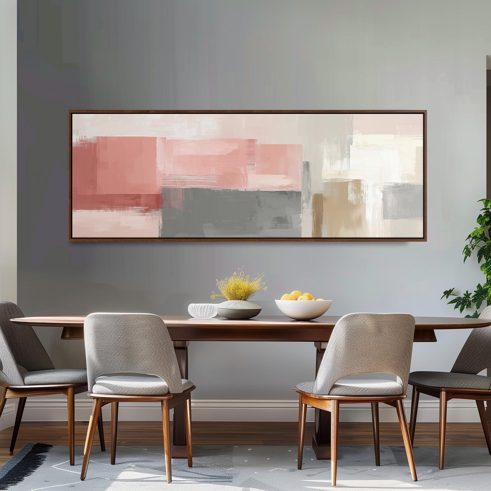 a modern dining room with a wooden table and four gray chairs. Above the table, there is a large abstract painting in shades of pink and gray. On the table, there is a bowl of fruit and a vase of flowers.