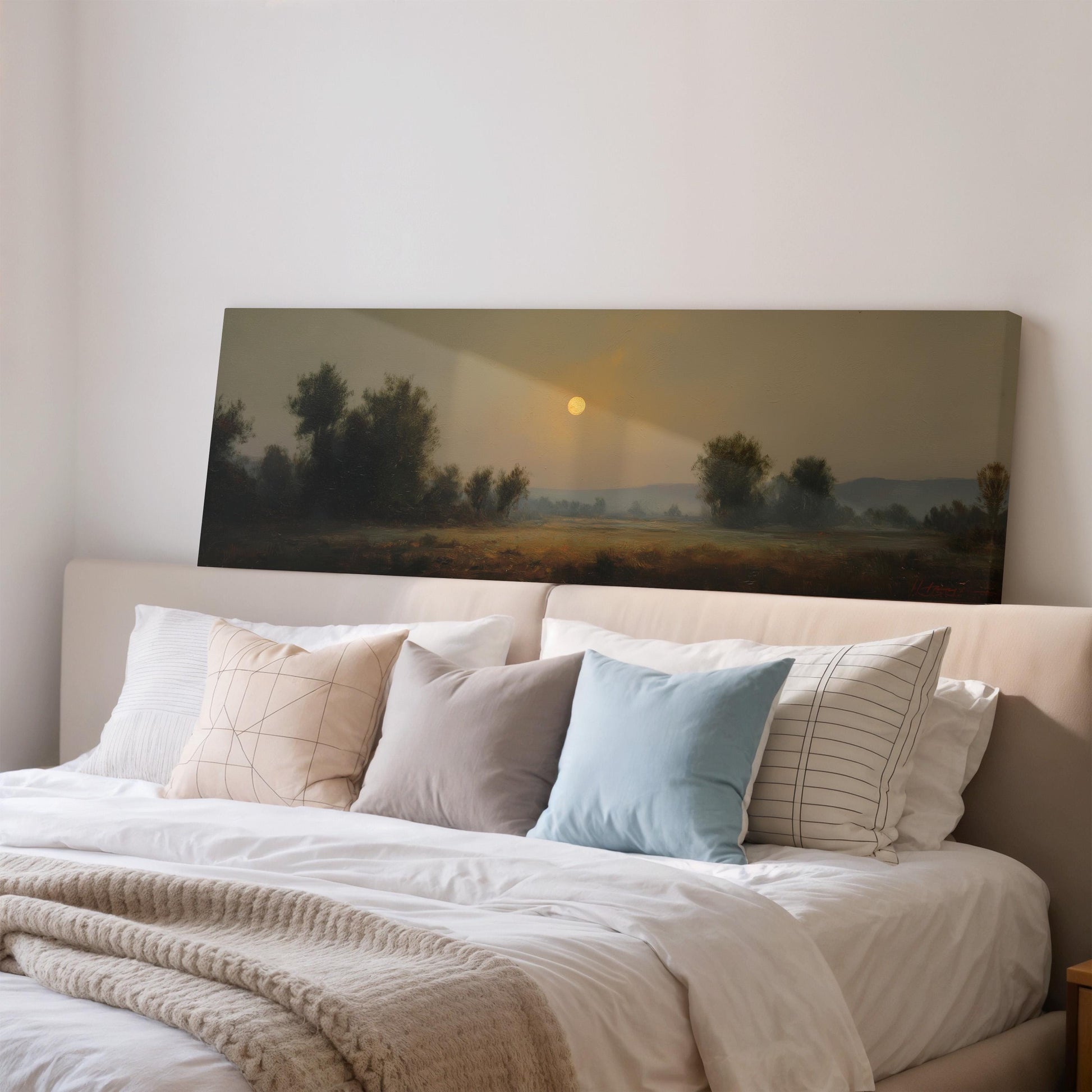 a large painting of a landscape with a sunset over a field, hanging above a bed with white pillows and a gray blanket.