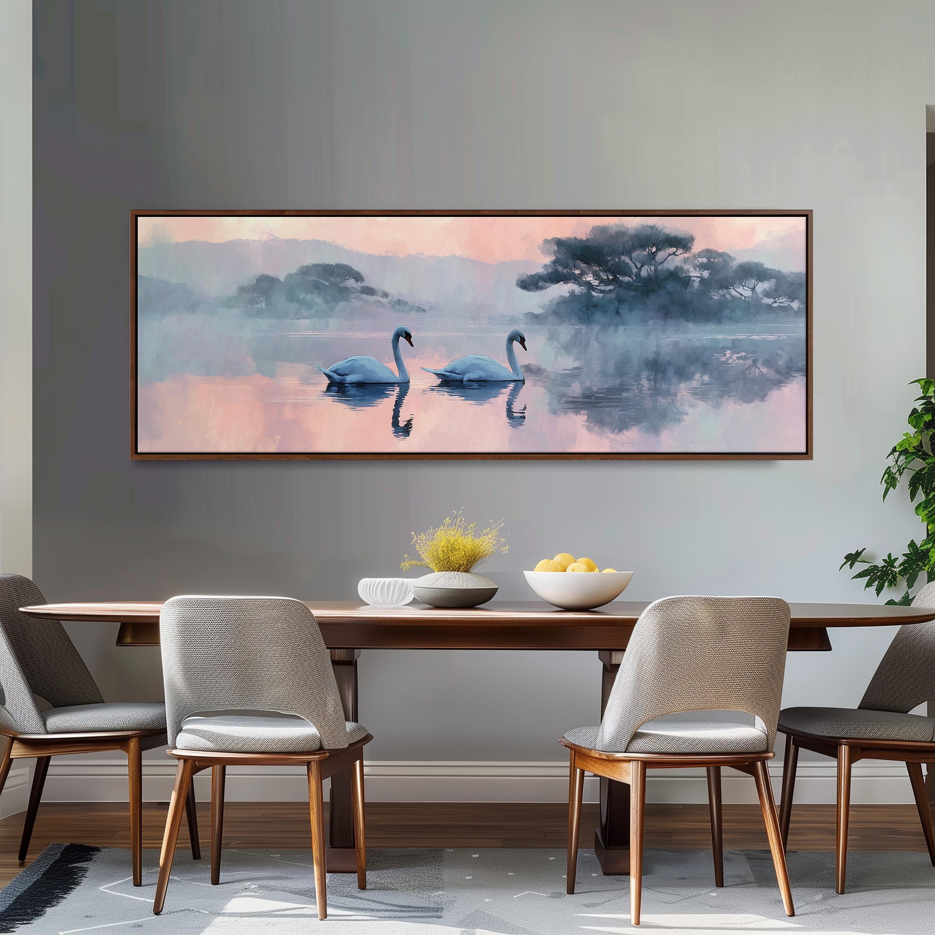 a large painting of two swans floating on a lake, with a misty background and a warm, pinkish hue. The painting is hung on a wall above a wooden dining table, which has four chairs around it. The table is set with a bowl of fruit and a vase of flowers, creating a cozy and inviting atmosphere.