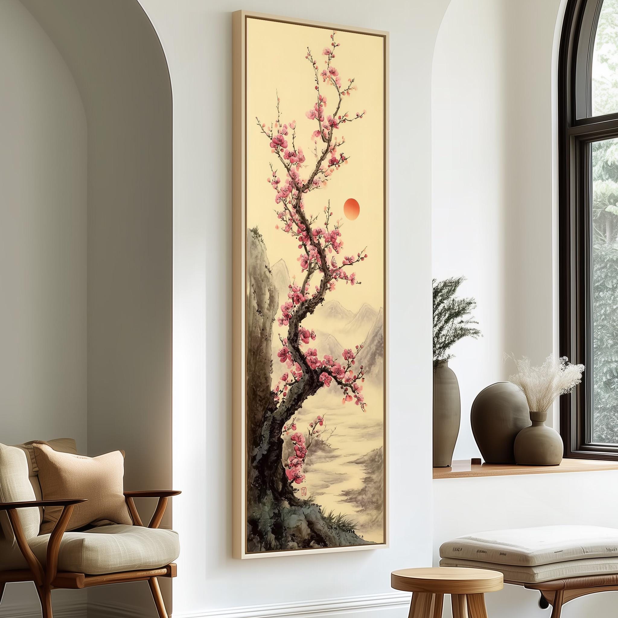 a large framed painting of a cherry blossom tree with pink flowers, hanging on a wall in a room with a wooden chair and a small table.