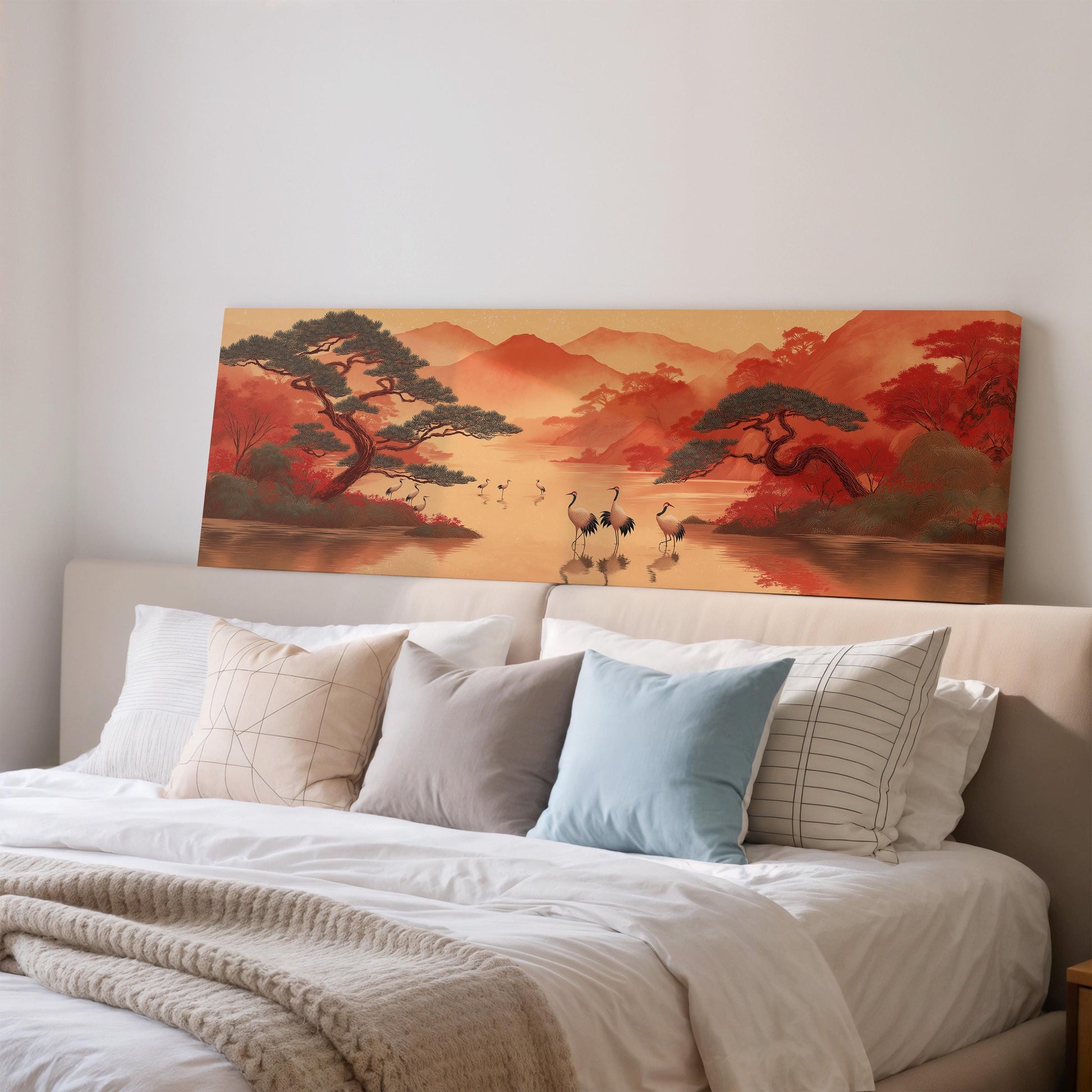 a large painting of a serene landscape with a river, mountains, and trees, hanging above a bed with white pillows and a gray blanket.