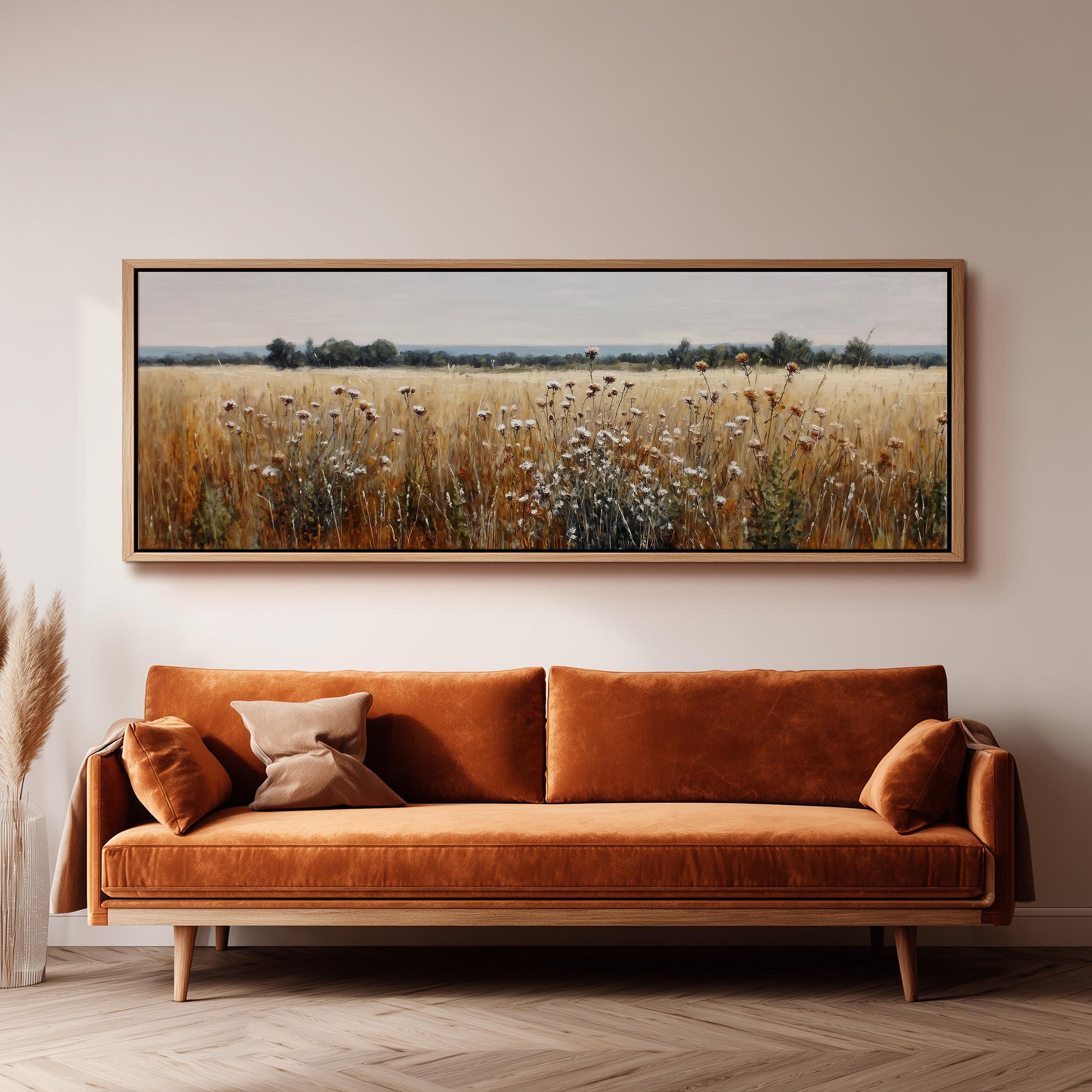 a large, framed painting of a field with tall grass and wildflowers hanging on a wall above a brown sofa.