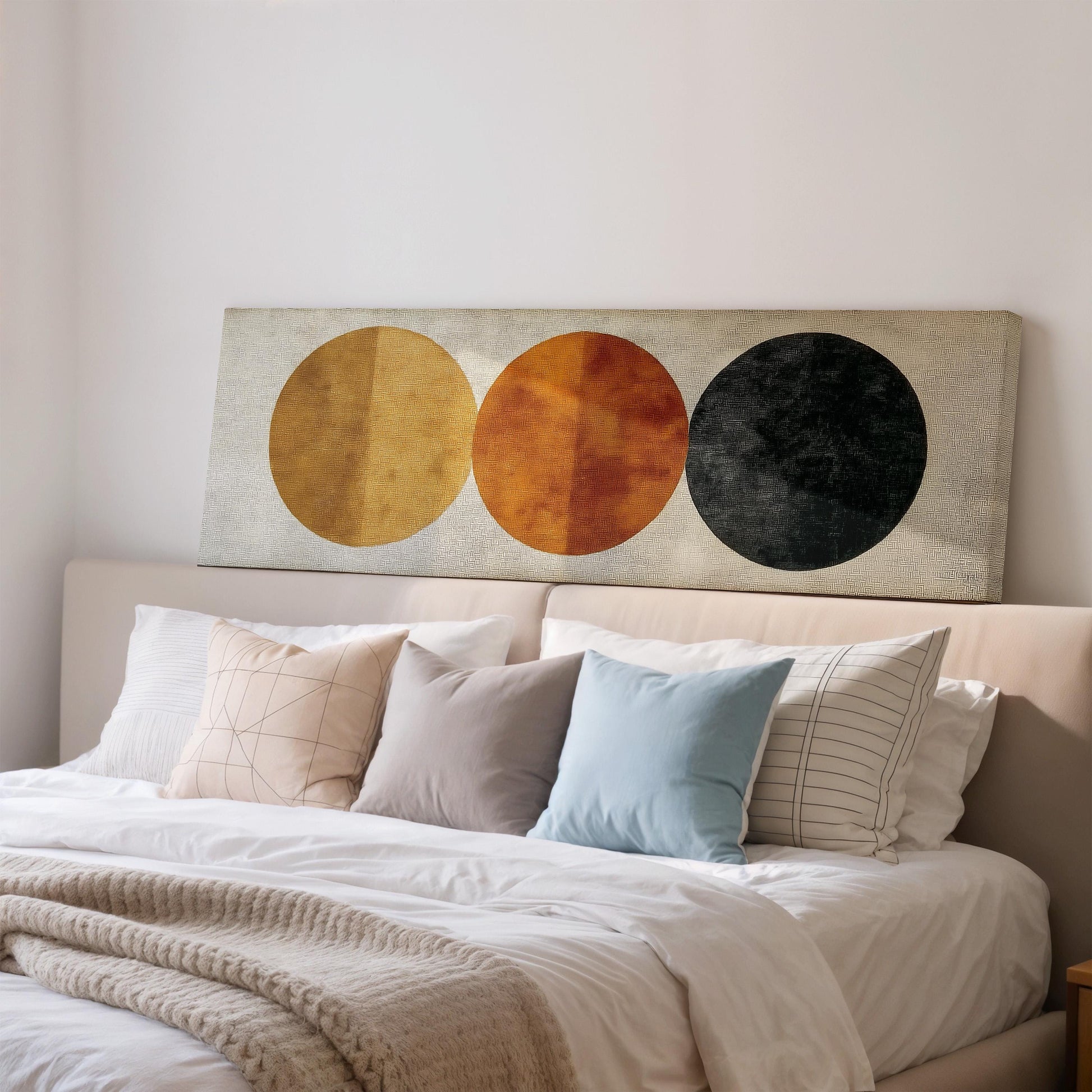 a well-made bed with a variety of pillows and a blanket, and a large abstract painting featuring three circles on the wall above the bed.