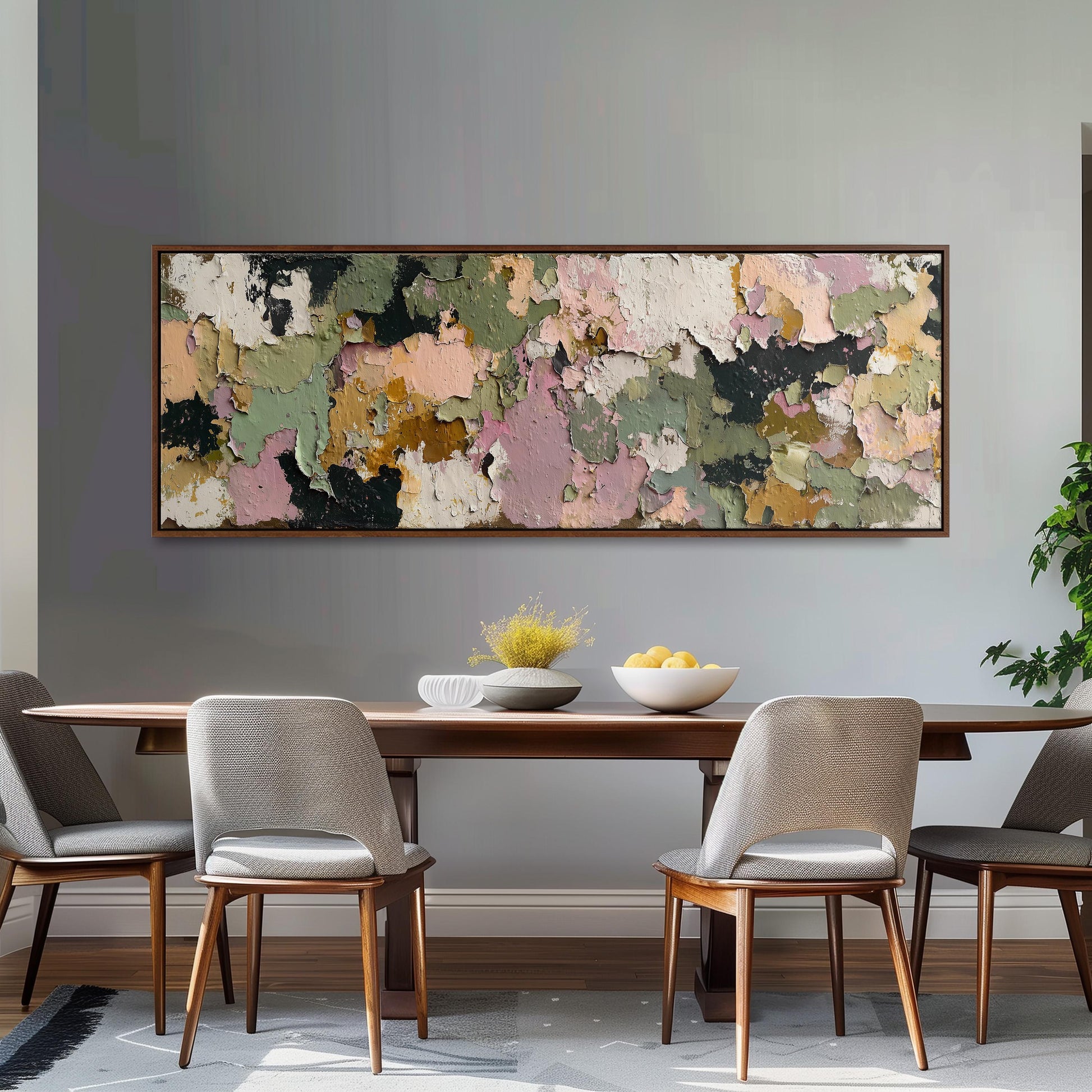 a dining room with a wooden table and four chairs. Above the table, there is a large, colorful painting hanging on the wall. The table is set with a bowl of fruit and a vase of flowers, creating a welcoming and inviting atmosphere.