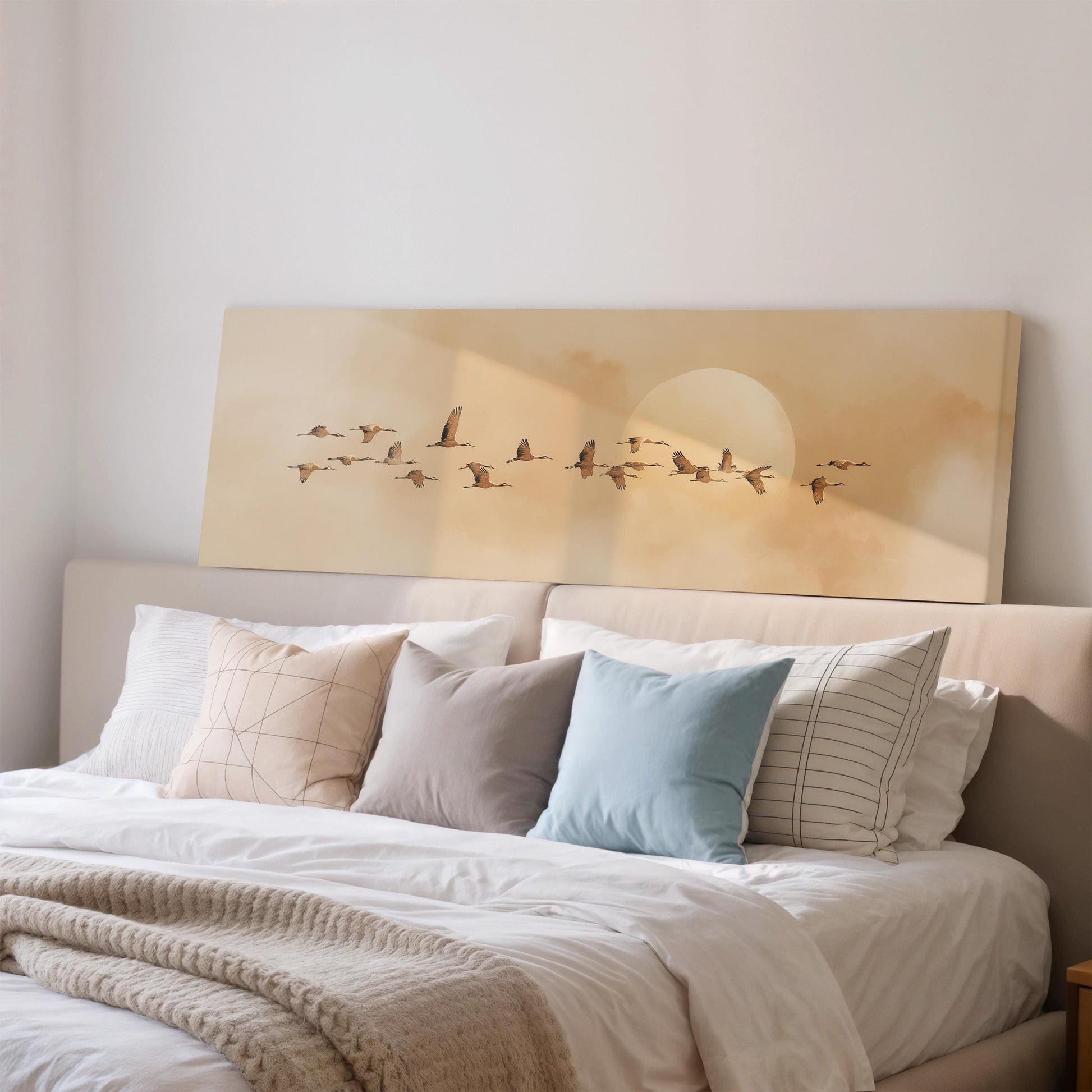 a cozy bedroom scene with a large bed adorned with white linens and a variety of colorful pillows. Above the bed, a large canvas print features a flock of birds flying across a cloudy sky.
