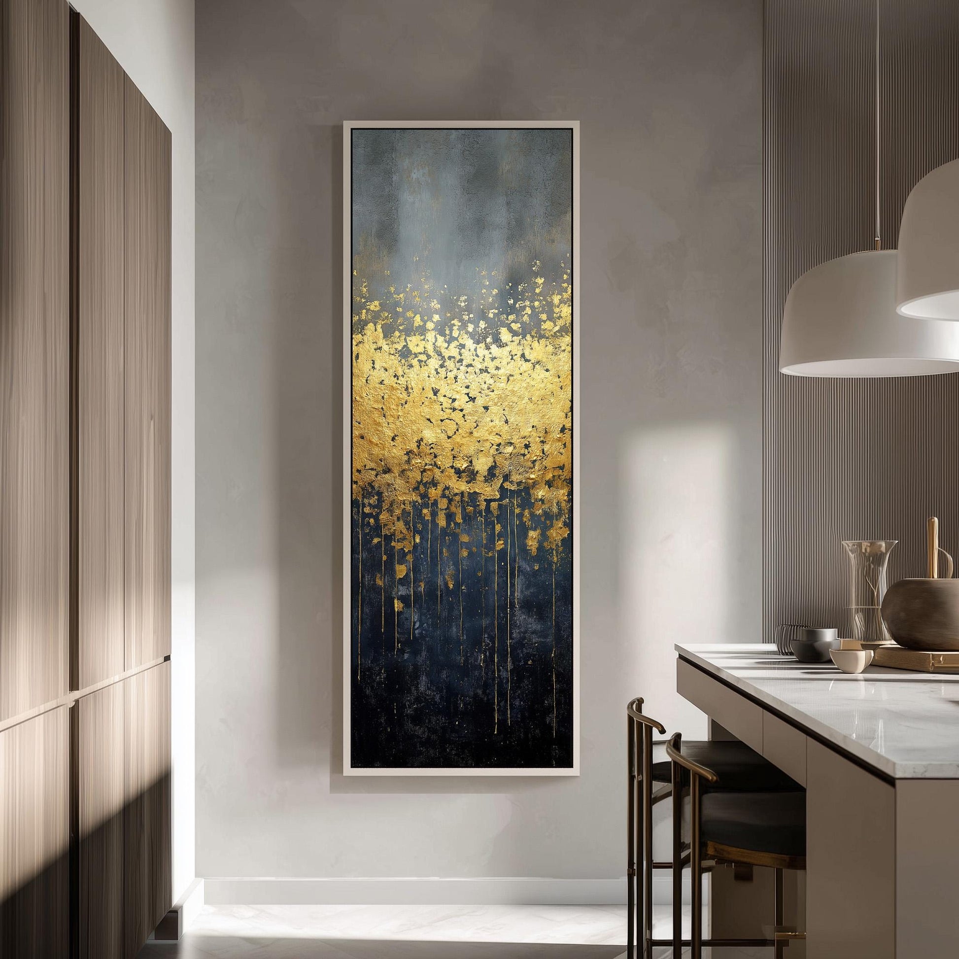 a modern kitchen with a large, abstract painting hanging on the wall. The painting has a dark blue background with a gold and black abstract design, creating a striking contrast. The kitchen is well-lit, with a white countertop and a wooden cabinet visible. There are also some chairs and a table in the room, suggesting a dining or relaxation area.
