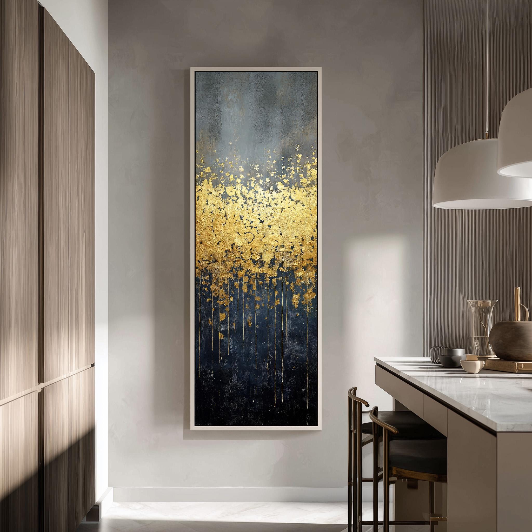 a modern kitchen with a large, abstract painting hanging on the wall. The painting has a dark blue background with a gold and black abstract design, creating a striking contrast. The kitchen is well-lit, with a white countertop and a wooden cabinet visible. There are also some chairs and a table in the room, suggesting a dining or relaxation area.