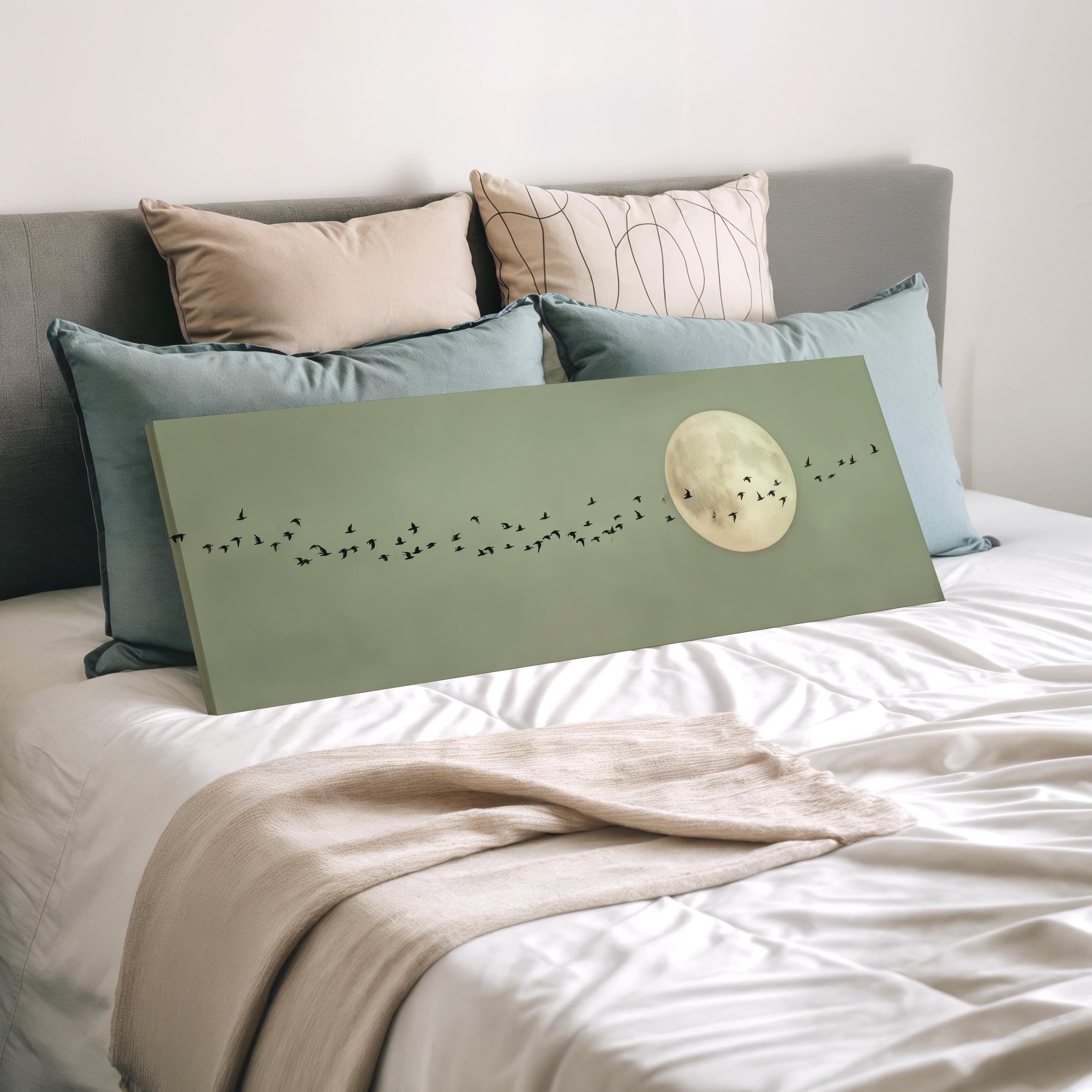 a bedroom with a bed and a large green canvas with a moon and birds on it. The bed is covered with white sheets and has several pillows on it.