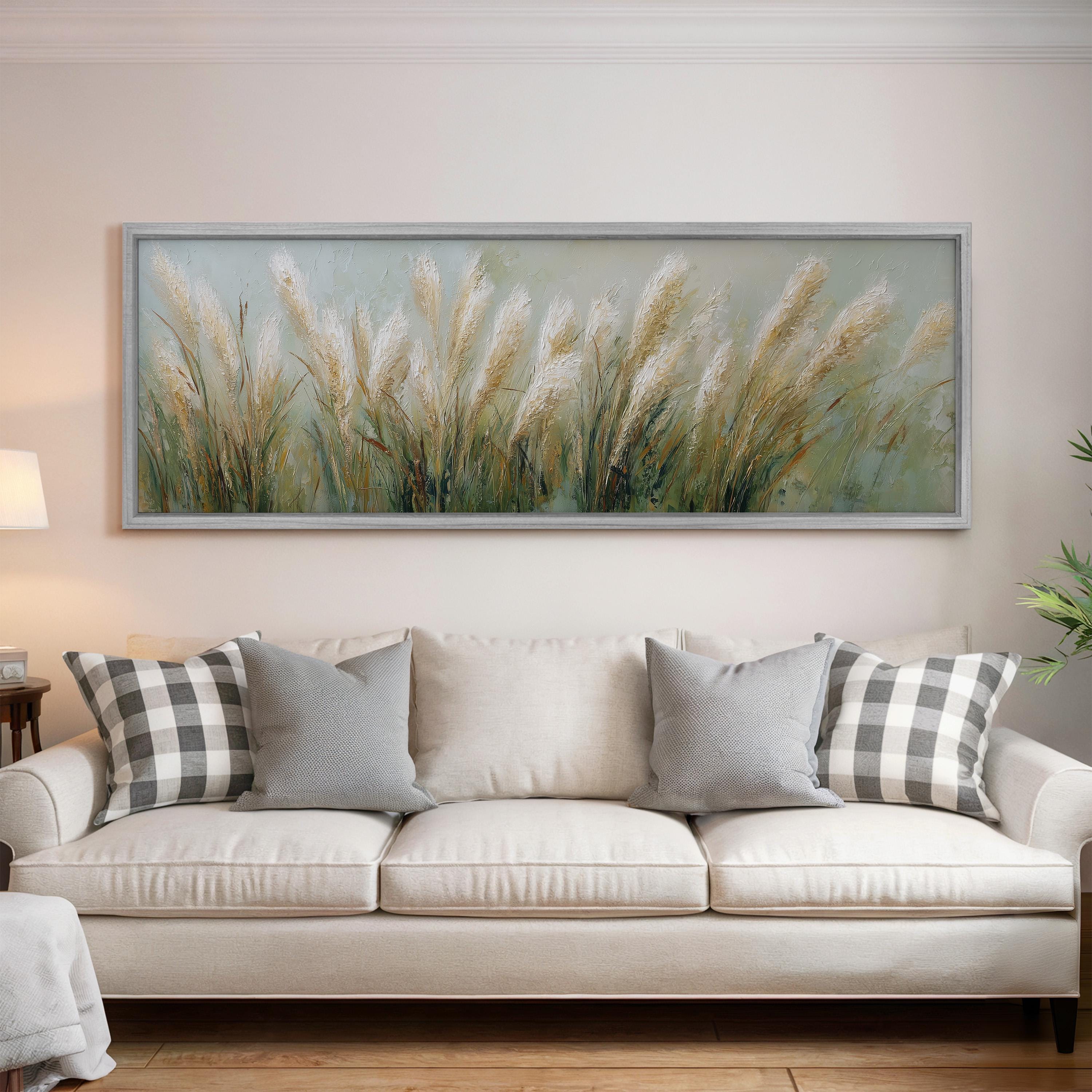 a large painting of tall grass hanging on a wall above a white sofa with gray and white patterned pillows.