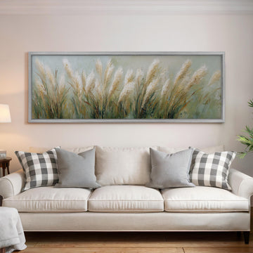 a large painting of tall grass hanging on a wall above a white sofa with gray and white patterned pillows.