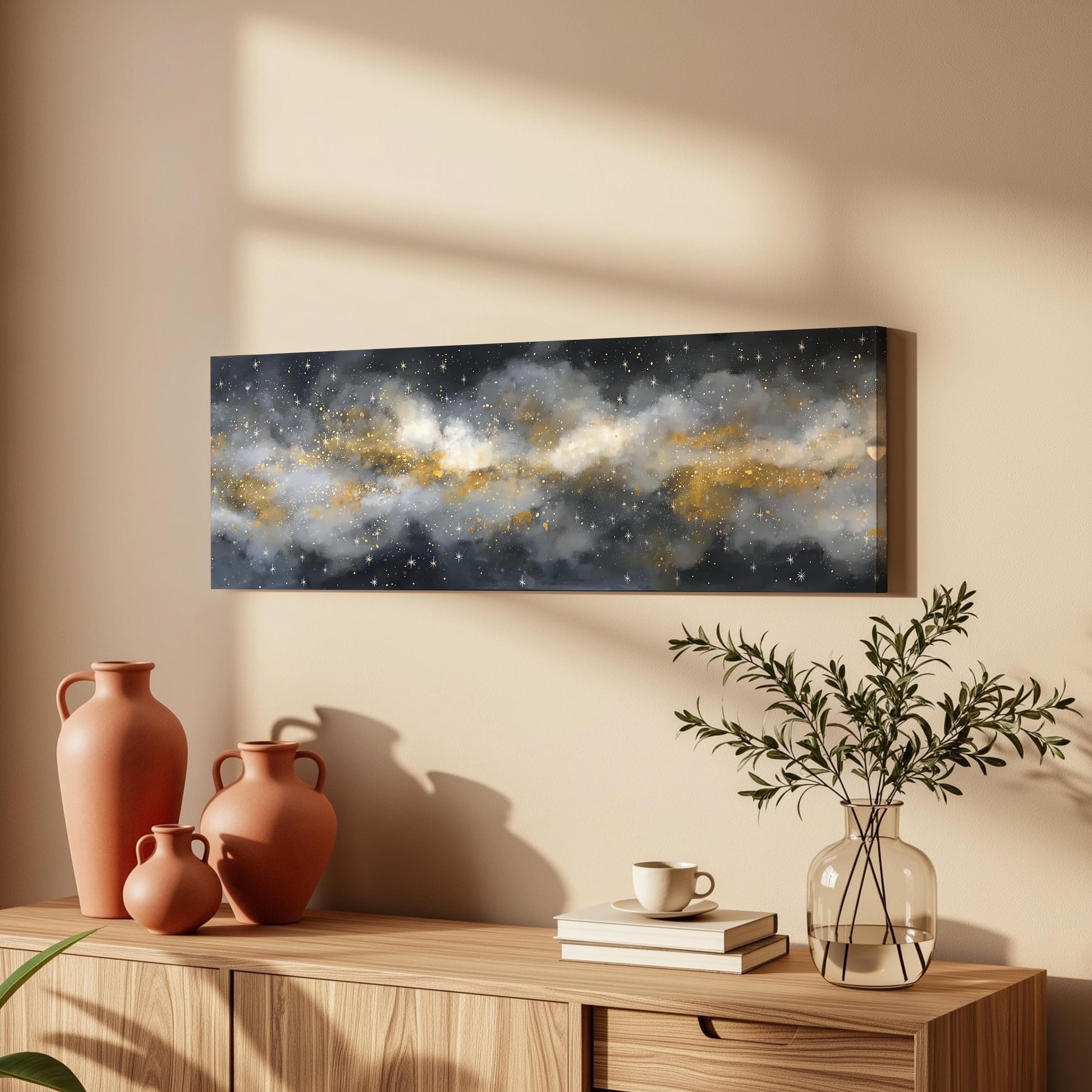 a wooden cabinet with a vase of greenery, a coffee cup, and a stack of books on top. Above the cabinet, there is a framed painting depicting a starry night sky with a galaxy-like pattern.
