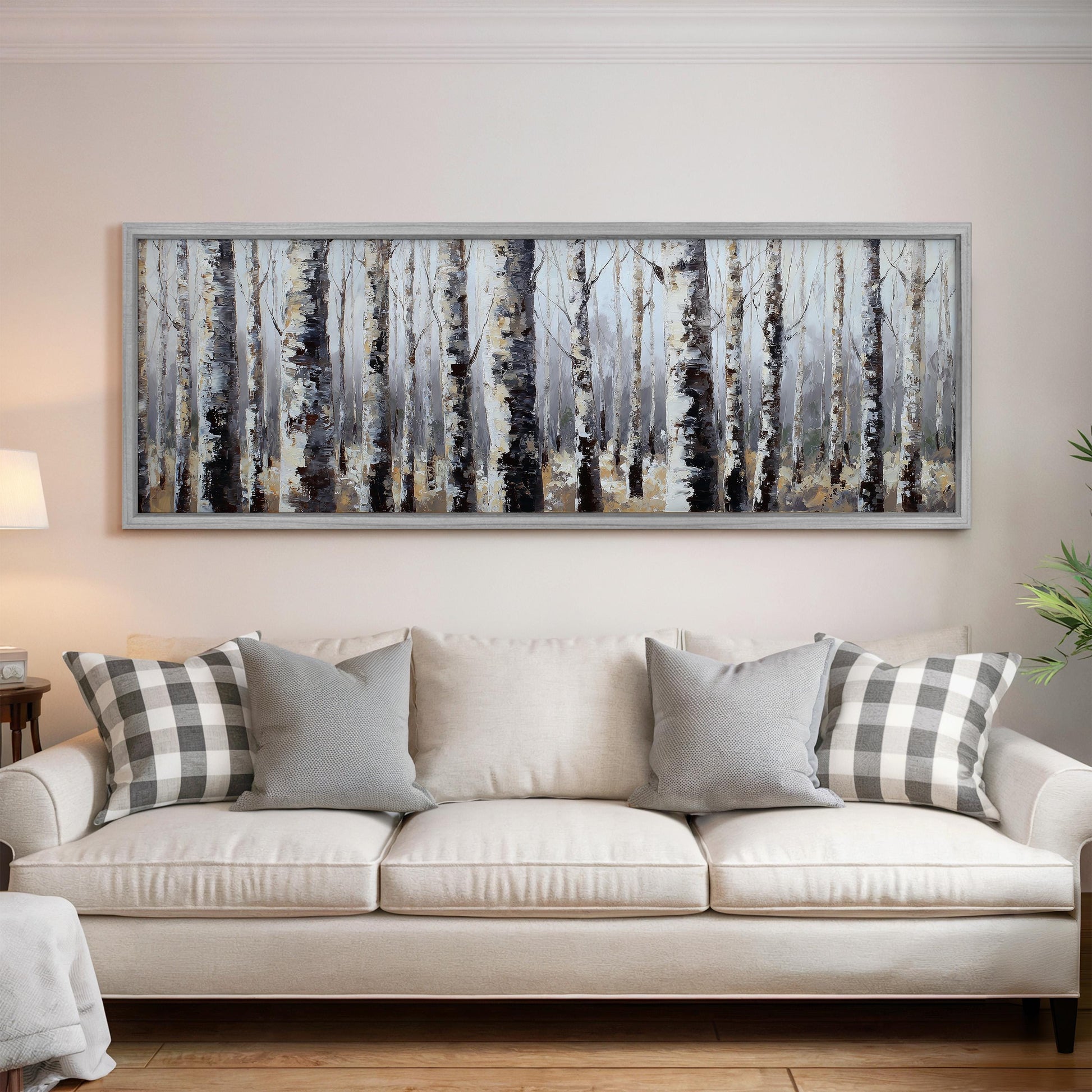 a large, framed painting of a forest scene hanging on a wall above a white couch with gray and white pillows.