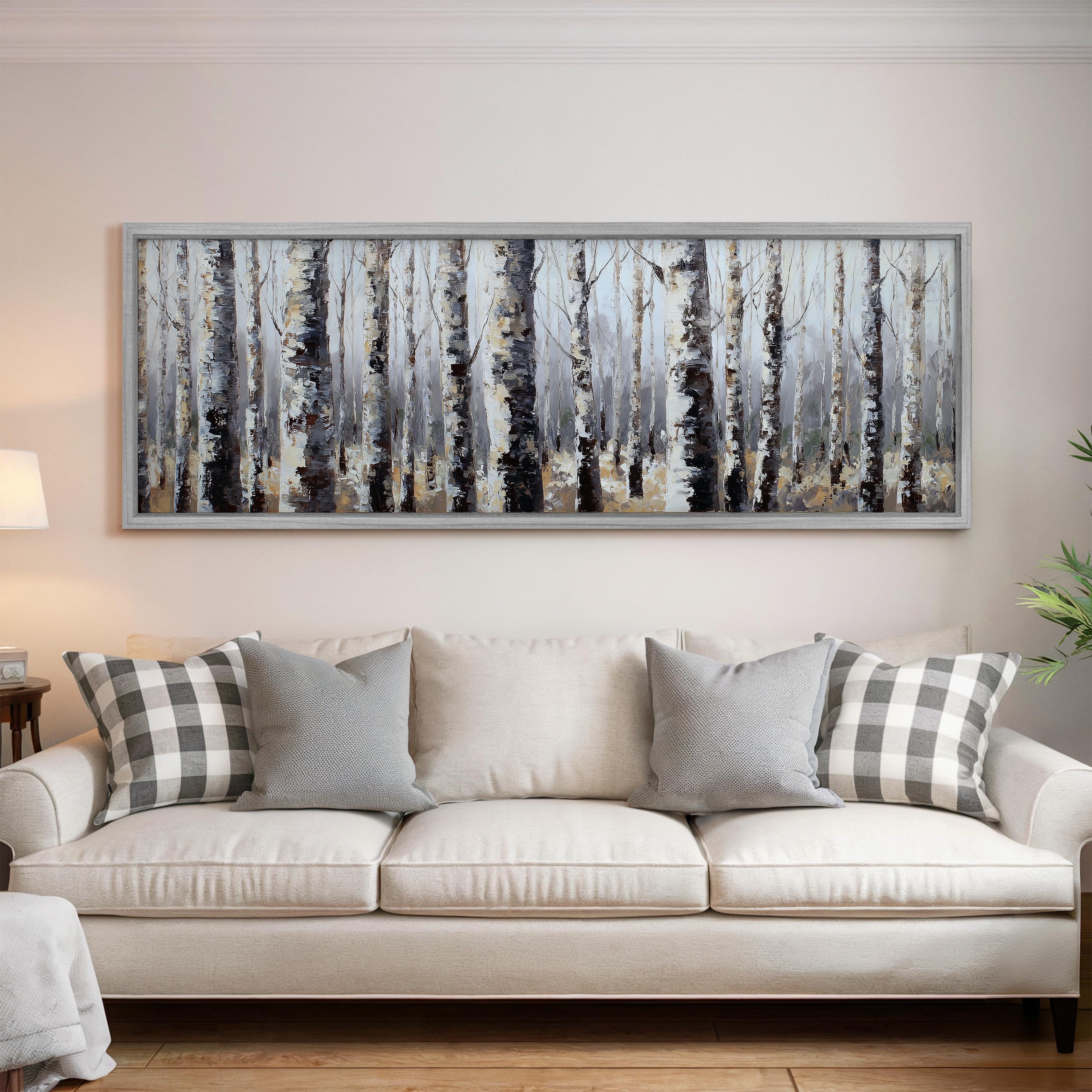 a large, framed painting of a forest scene hanging on a wall above a white couch with gray and white pillows.