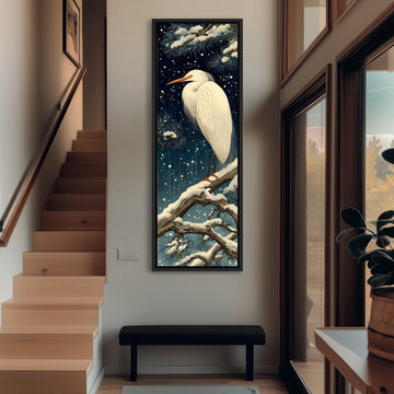 a large, framed painting of a white heron perched on a branch, set against a snowy night sky. The painting is hanging on a wall in a hallway, with a staircase visible in the background.