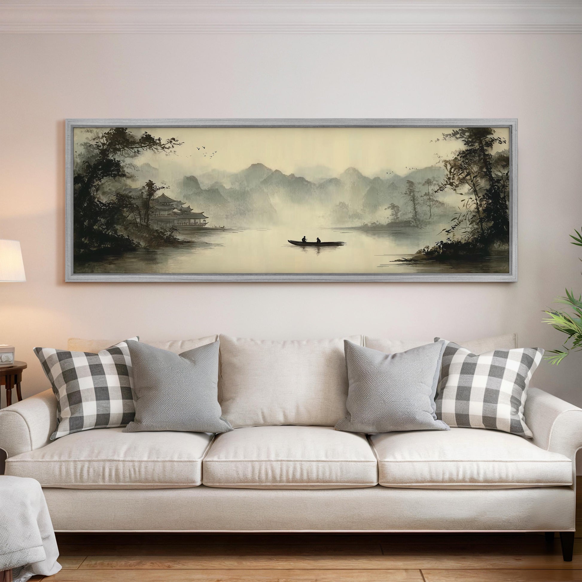 a large painting of a serene landscape with a boat on a lake, hanging on a wall above a white sofa with gray and white patterned pillows.