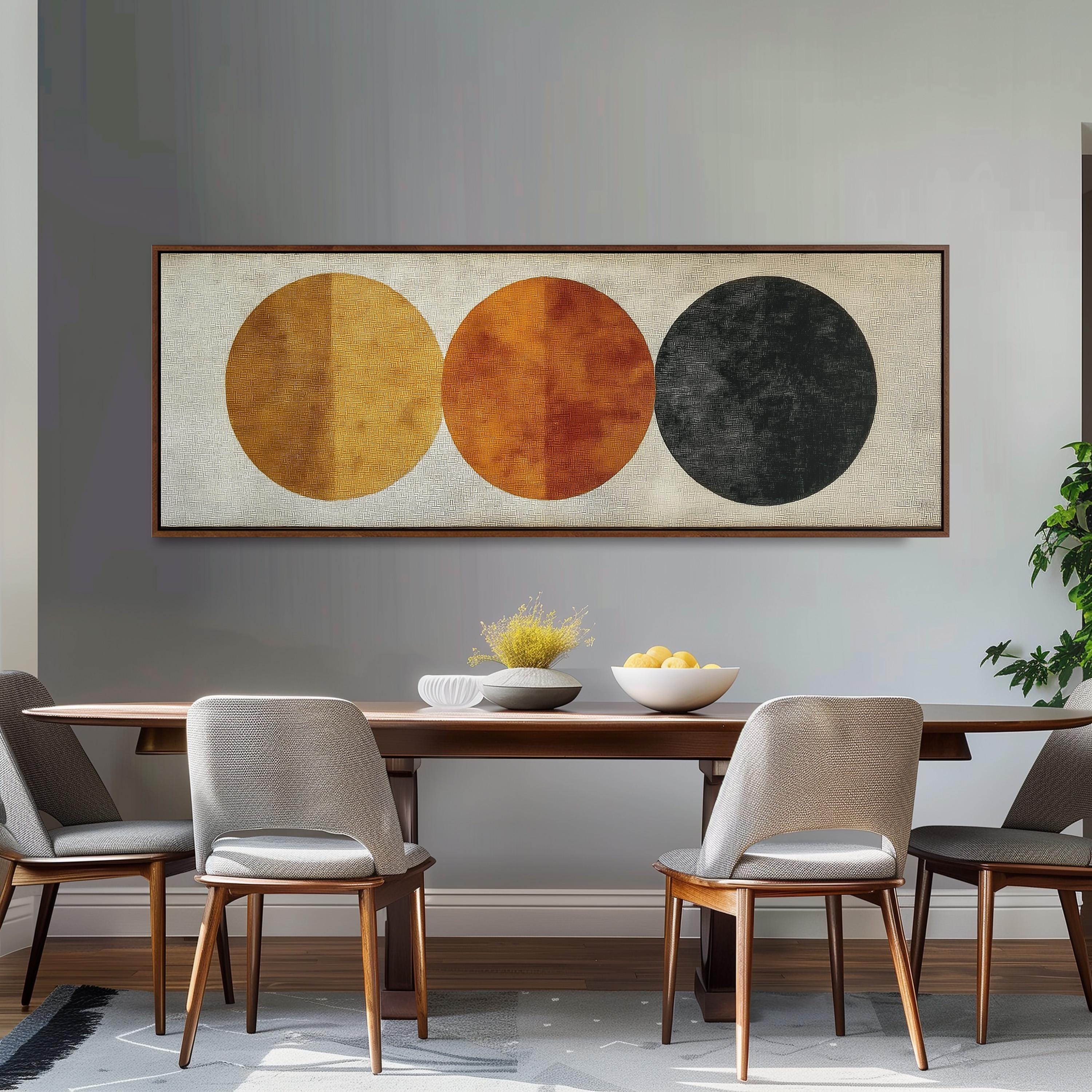 a modern dining room with a wooden table and four chairs. Above the table, there is a large abstract painting with three circles in different colors - yellow, orange, and black. The table is set with a bowl of fruit and a vase of flowers, creating a warm and inviting atmosphere.