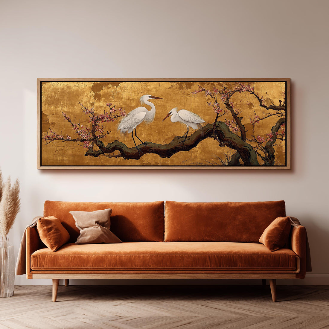a large, ornate painting of two white birds perched on a branch with pink flowers, hanging on a wall above a brown sofa.