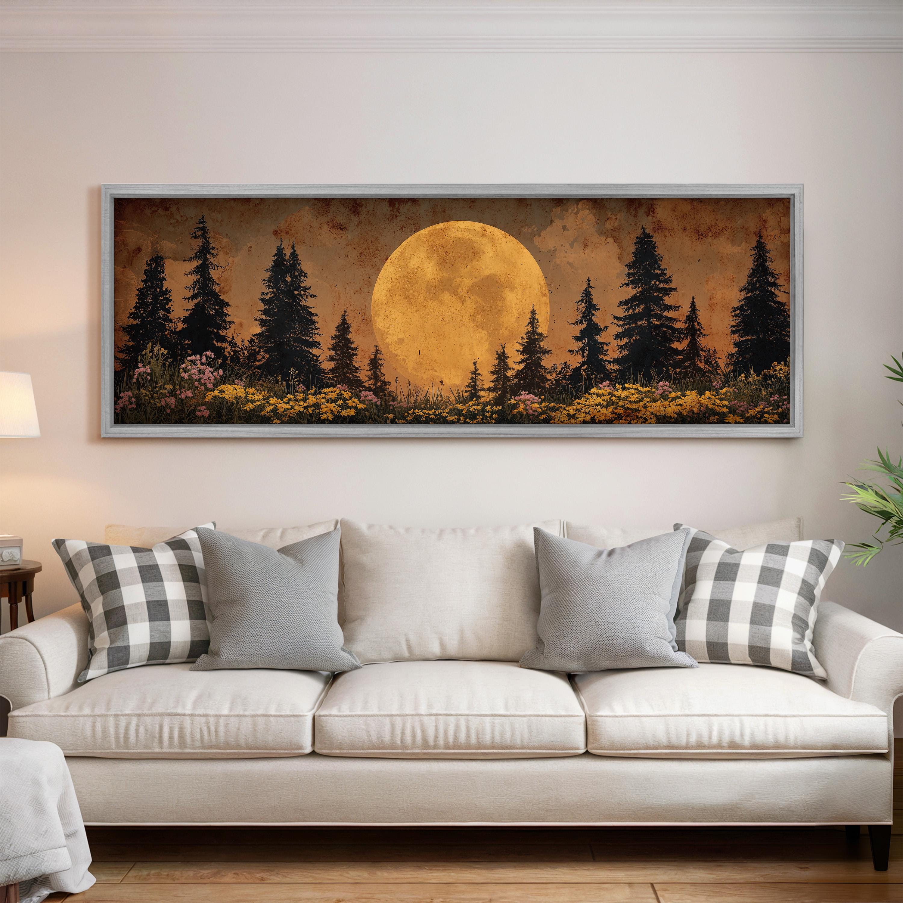 a large framed painting of a forest scene with a full moon in the background, hanging on a wall above a white sofa with gray and white plaid throw pillows.