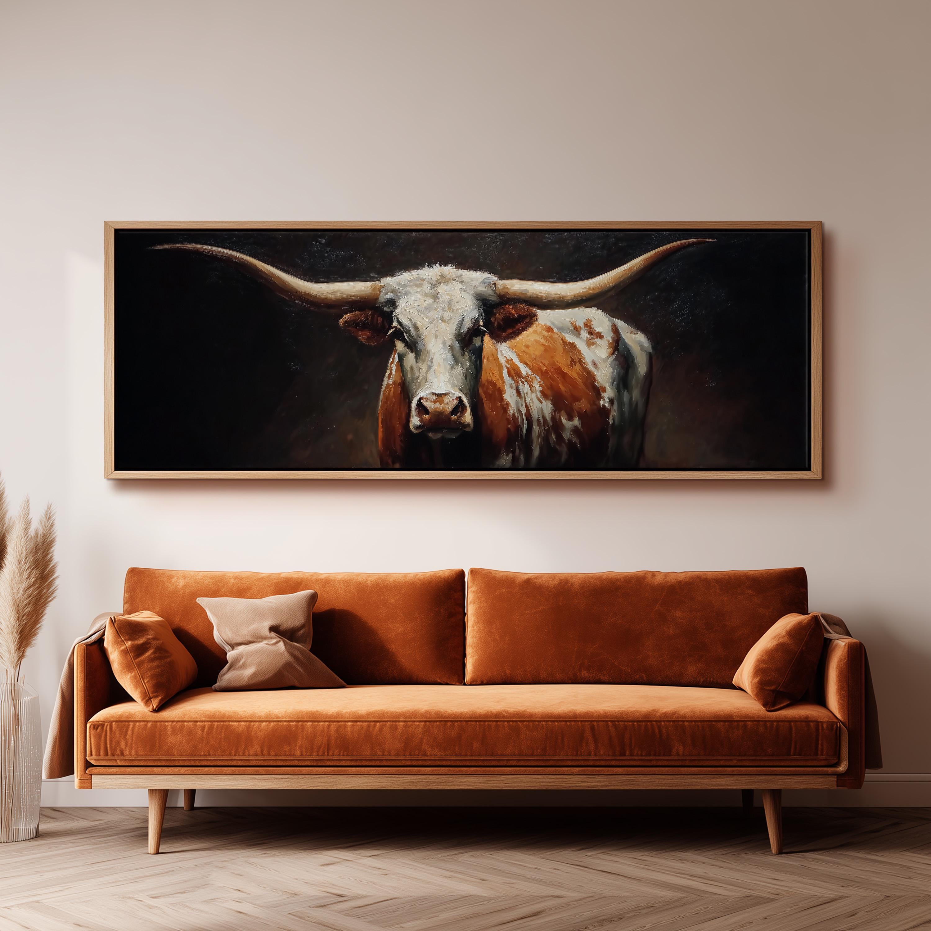 a large painting of a bull with long horns hanging on a wall above a brown sofa.