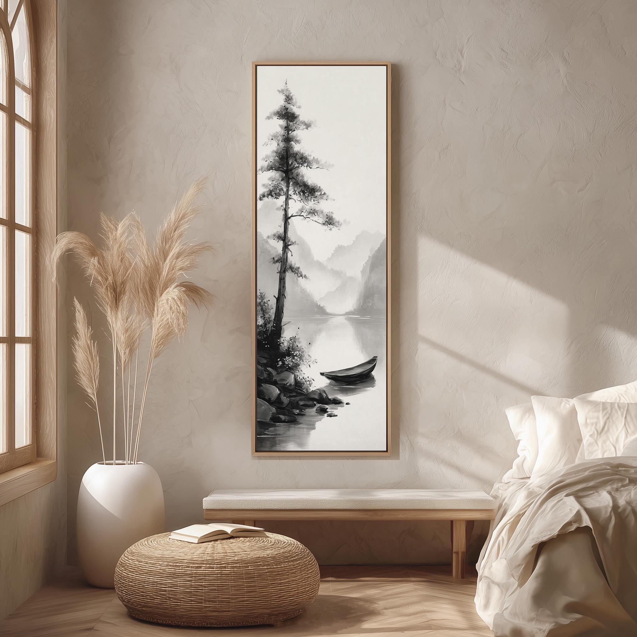a serene bedroom scene with a large black and white landscape painting hanging on the wall, depicting a boat on a lake surrounded by mountains. The painting is framed in a wooden frame and is the focal point of the room. The room features a bed with white bedding, a wicker ottoman, and a potted plant, creating a cozy and inviting atmosphere.